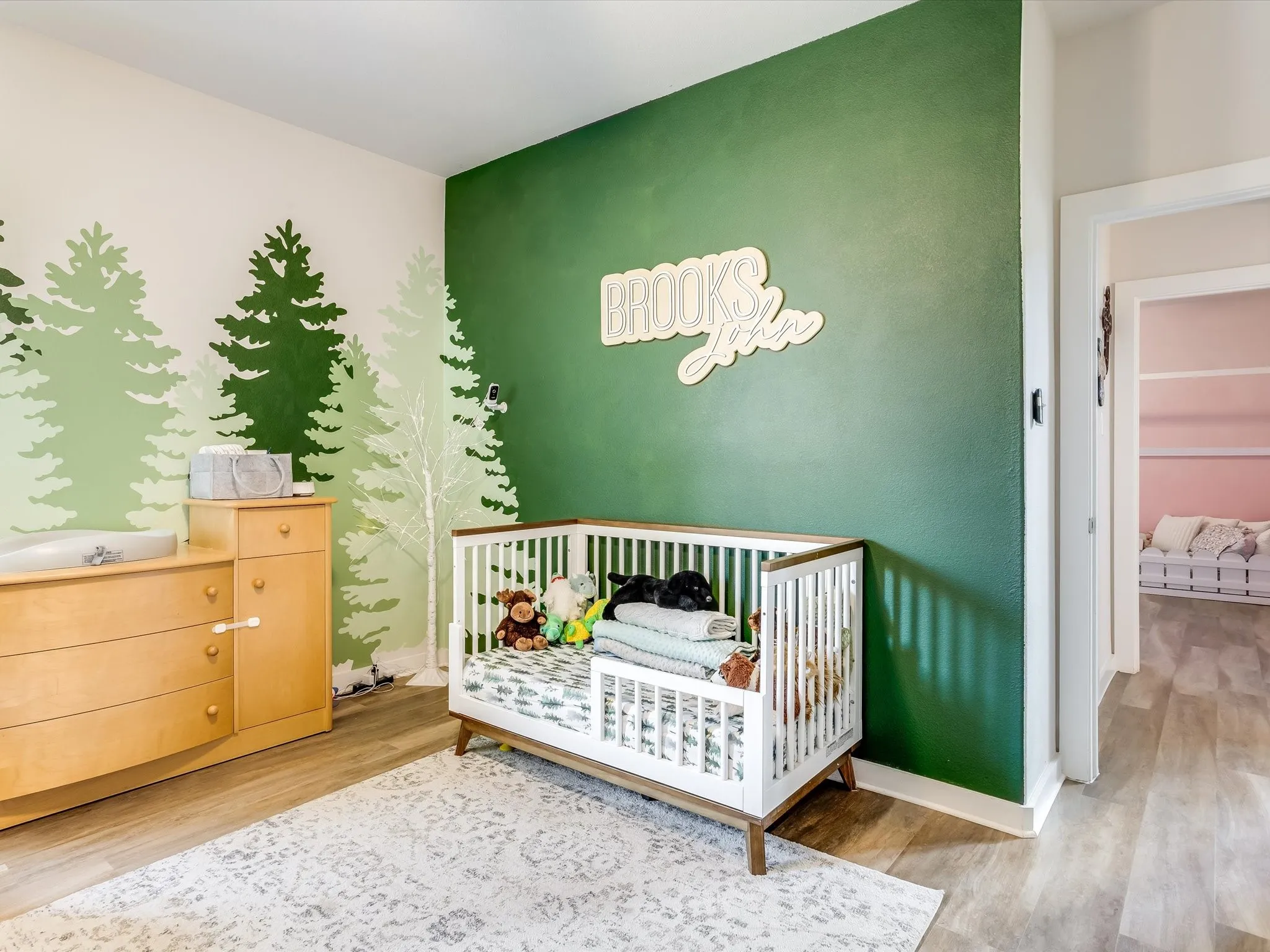 Spacious room featuring wood-finish flooring and a distinctive two-toned wall design with forest-themed graphics