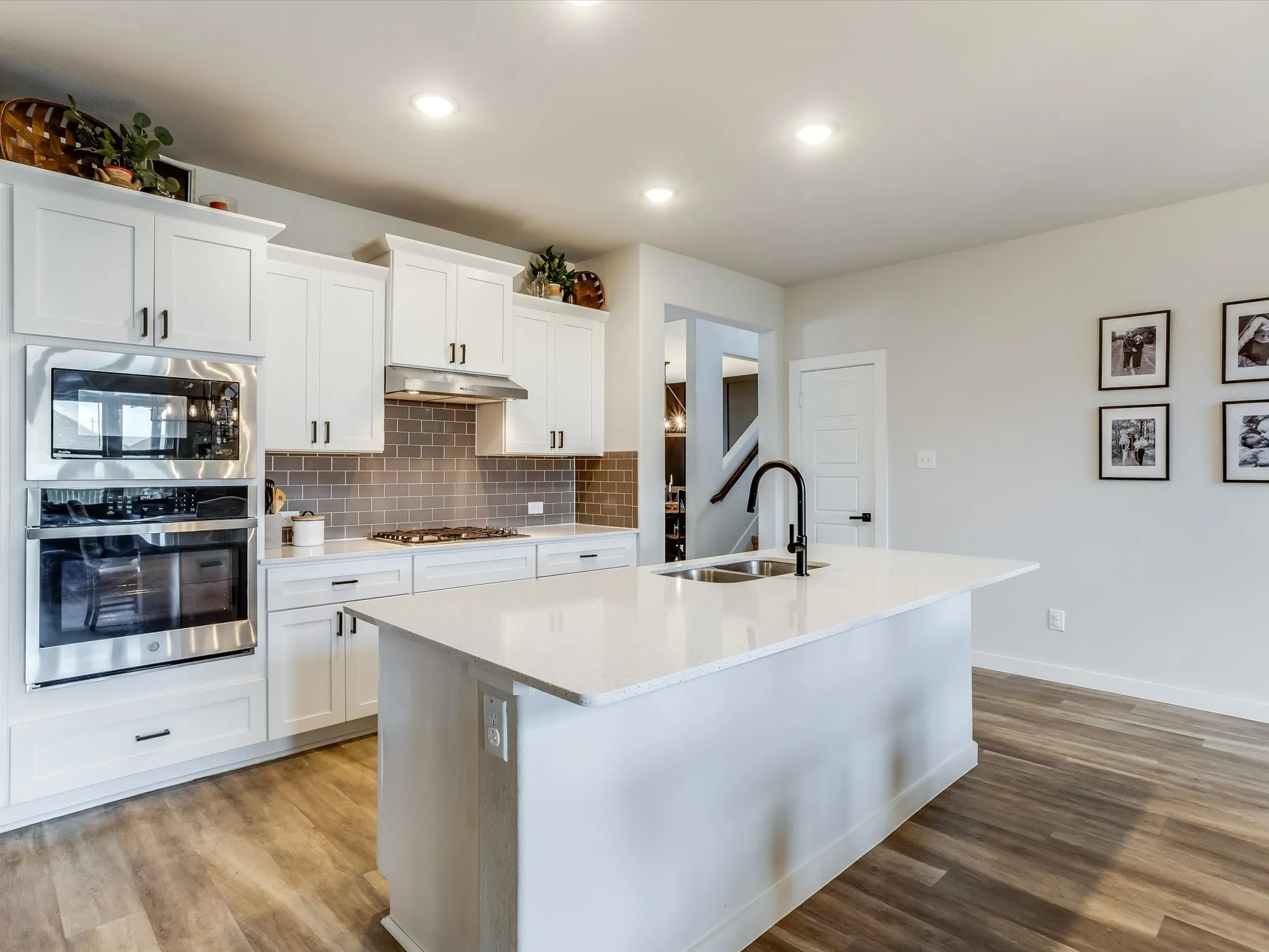 Kitchen featuring white cabinetry, stainless steel appliances including a built-in microwave and oven, a gray subway tile backsplash, a center island with a sink and matte black faucet, and wood-finish flooring