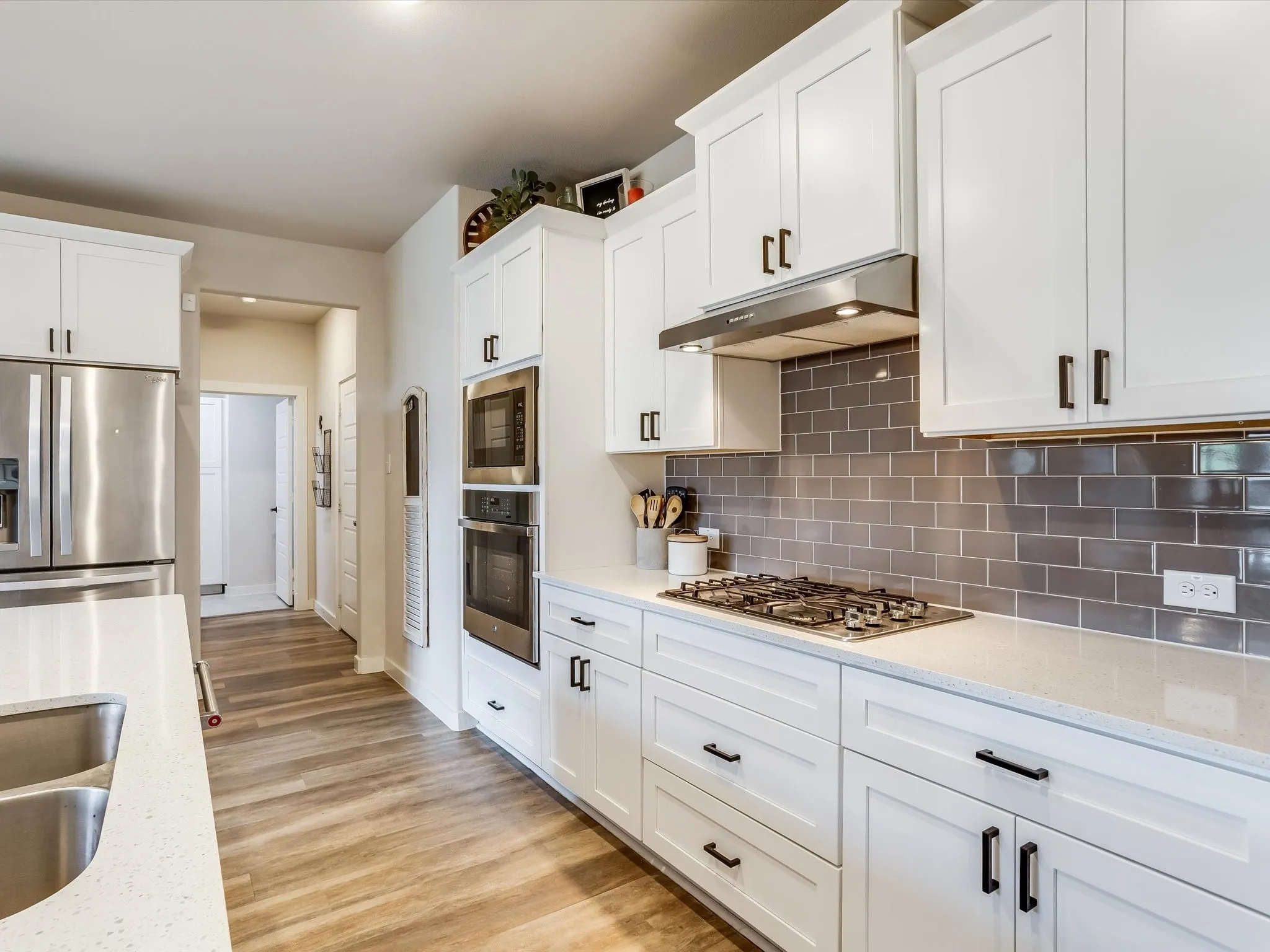 Kitchen featuring white cabinetry, stainless steel appliances, a subway tile backsplash, light-colored countertops, and wood-finish flooring