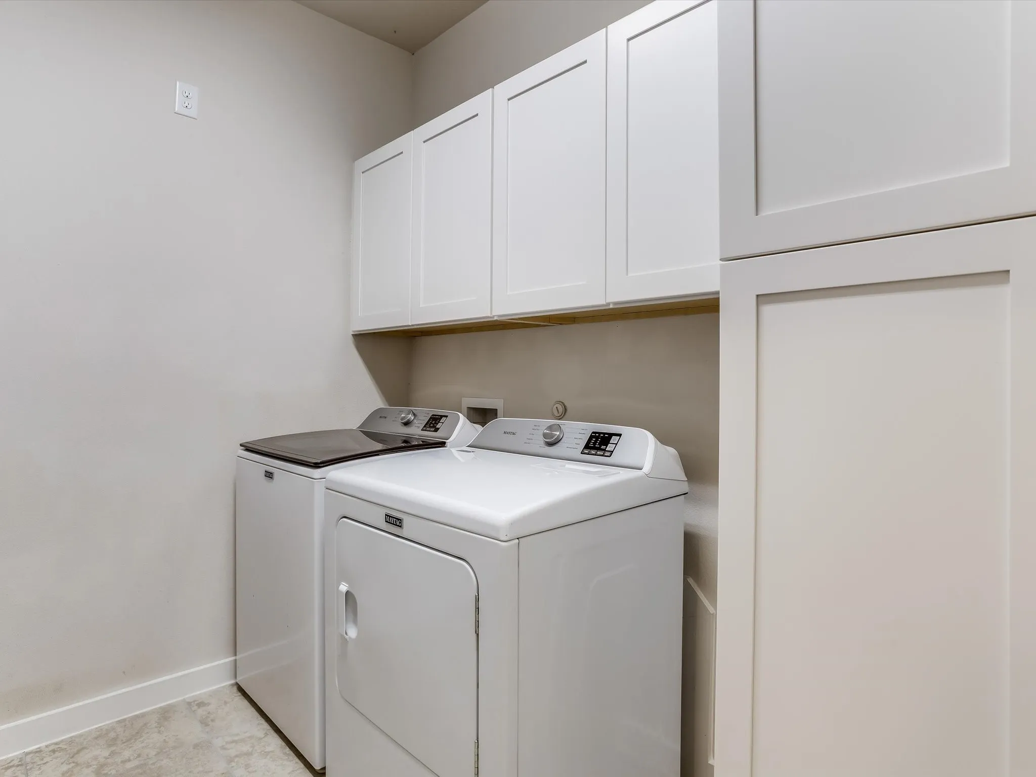 Laundry area featuring overhead white shaker cabinetry, an integrated tall storage cabinet, light-toned walls, and a durable tile floor