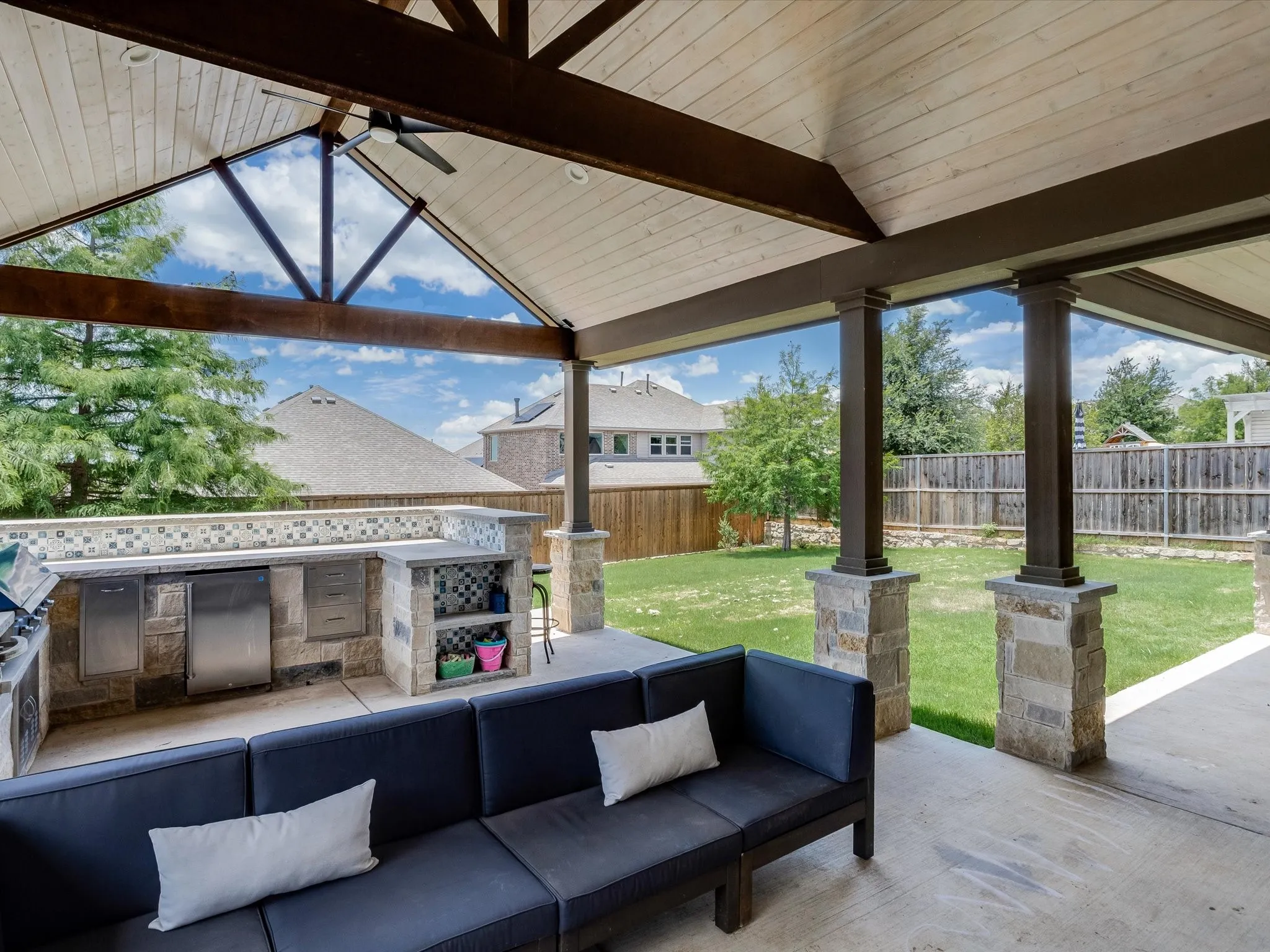 Expansive covered patio featuring a vaulted wood-plank ceiling, exposed wood beams, and a ceiling fan