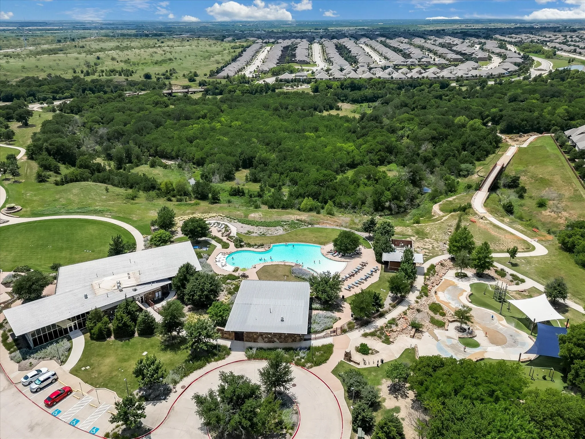 Expansive community amenities including a large swimming pool, adjacent lounge area with chaise seating, and a dedicated splash pad with shade structures