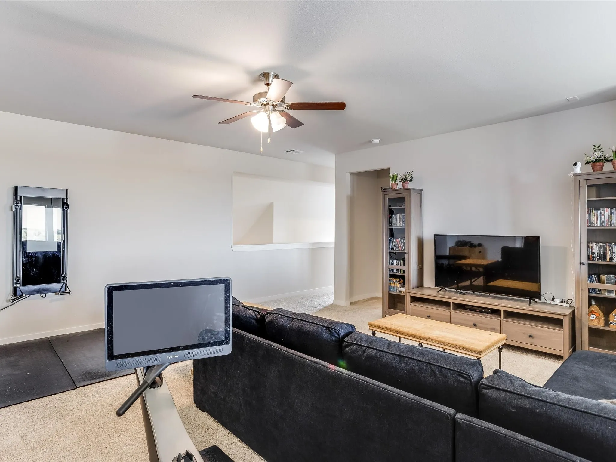 Spacious living area featuring light-toned walls, a ceiling fan with integrated lighting, and carpeted flooring