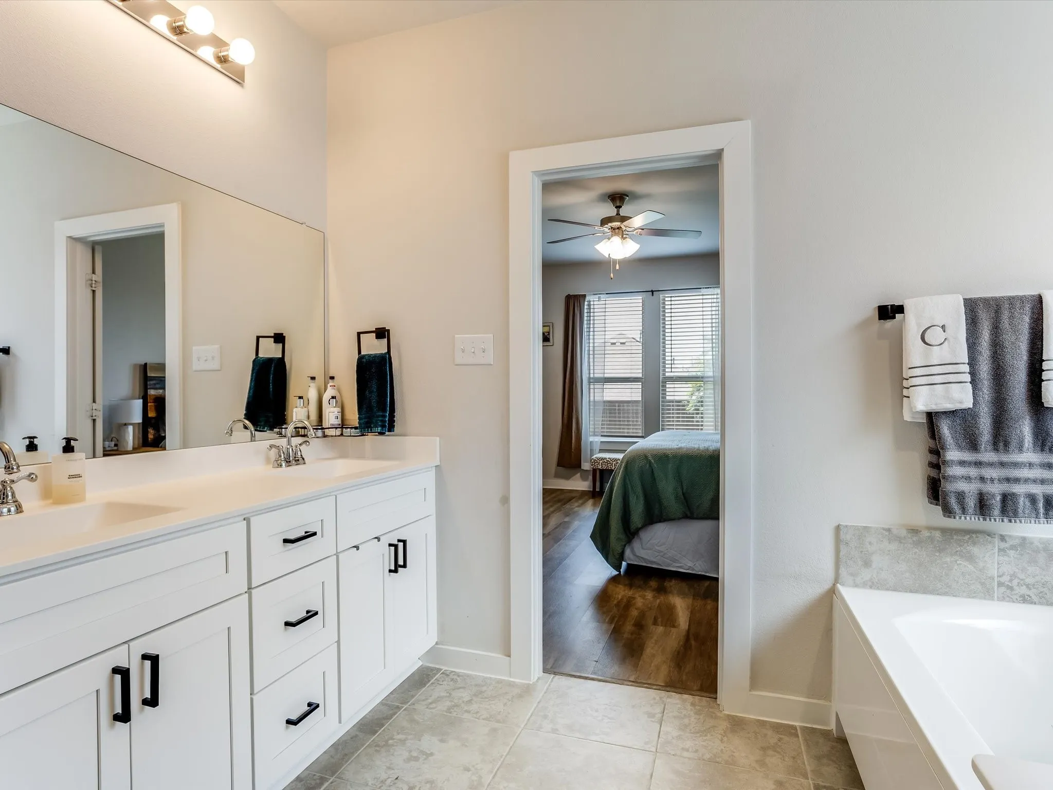 Bathroom vanity featuring dual sinks, white cabinetry with black hardware, and an expansive mirror