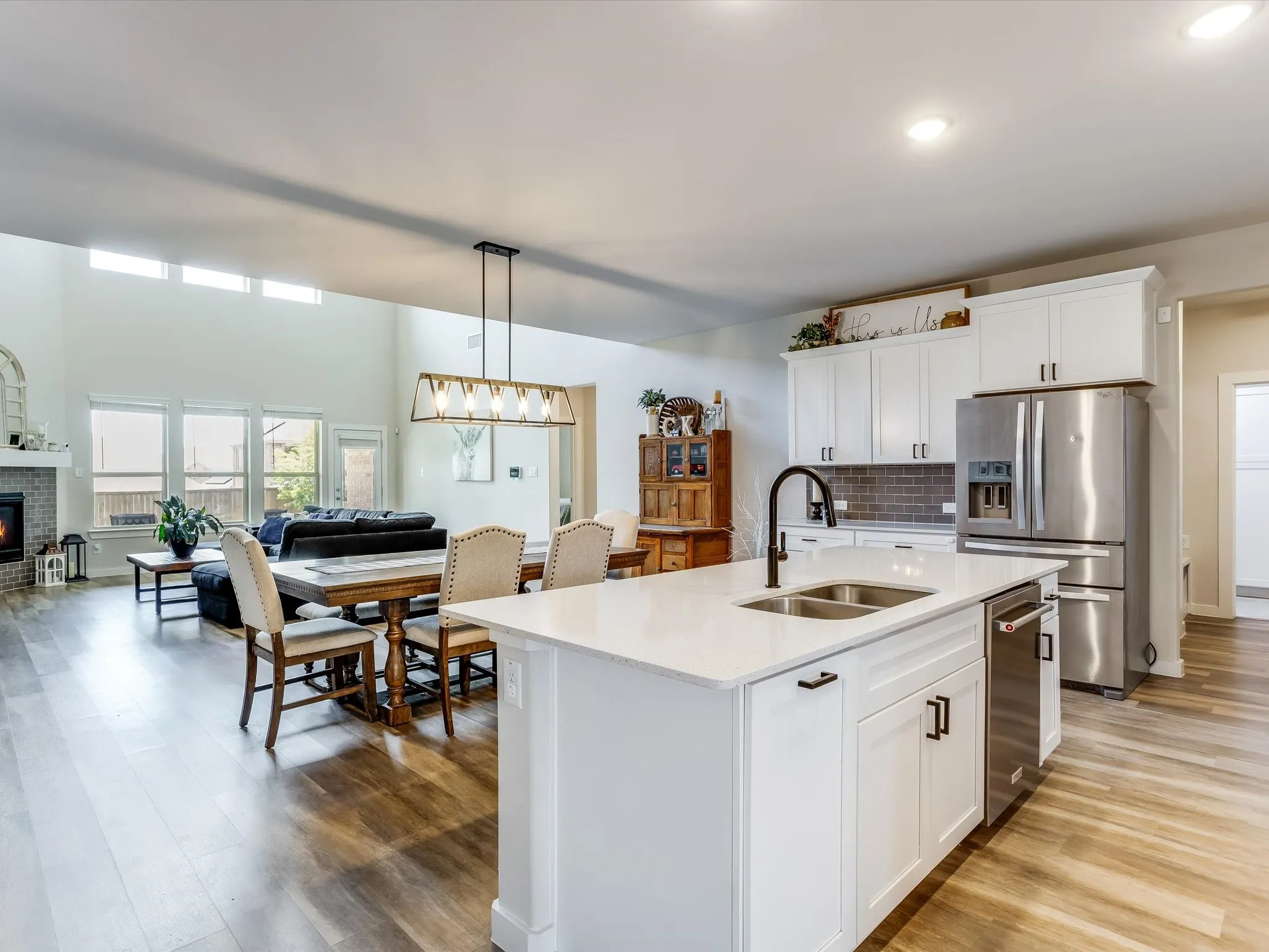 Open-concept living space featuring a central kitchen island with a double basin sink, white cabinetry, and stainless steel appliances