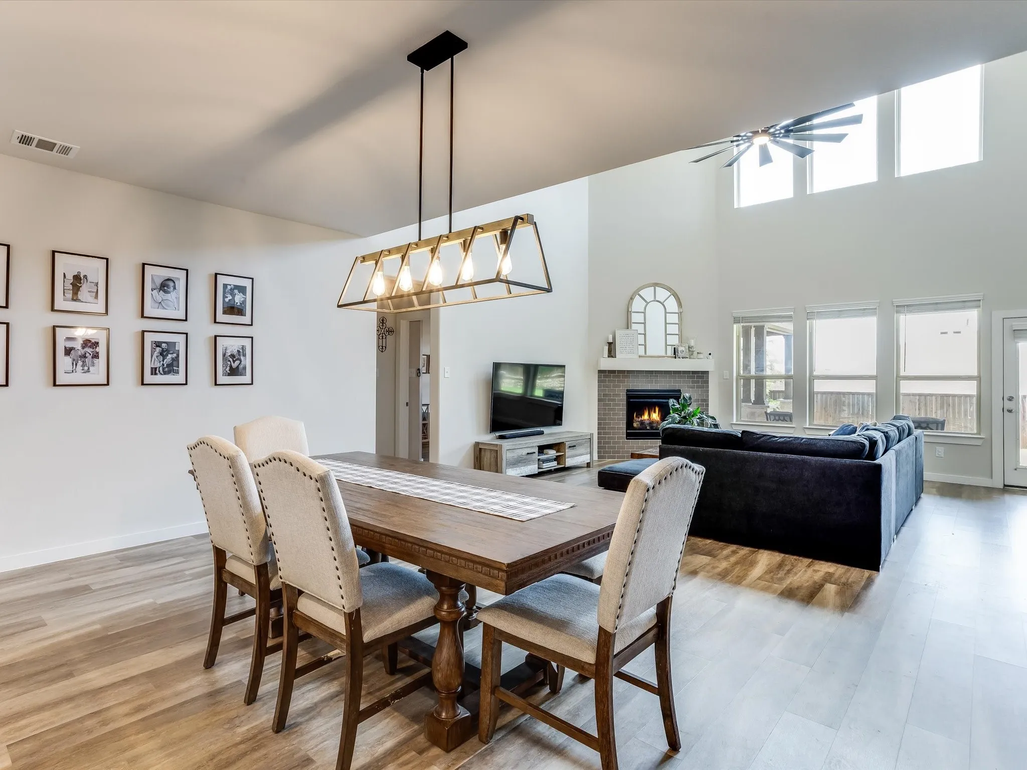 Open-concept living area featuring light wood-finish flooring, a two-story ceiling, and extensive natural light from multiple windows