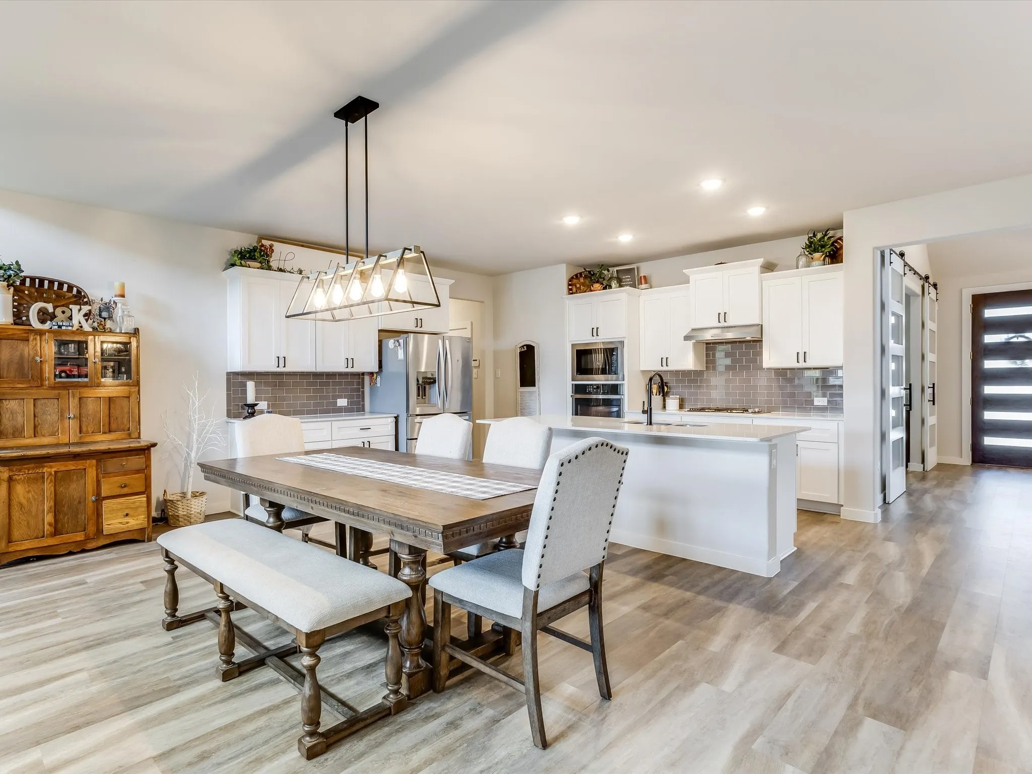 Expansive kitchen and dining area featuring light wood-finish flooring, white cabinetry, stainless steel appliances, a tiled backsplash, and recessed lighting