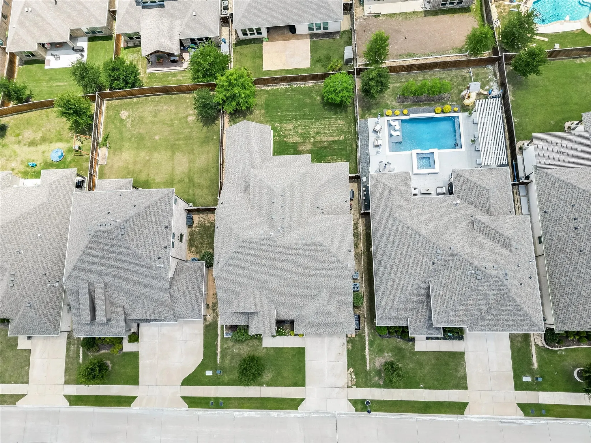 Aerial view showcasing the property's gray shingle roof, concrete driveway, and a fenced backyard with green lawn