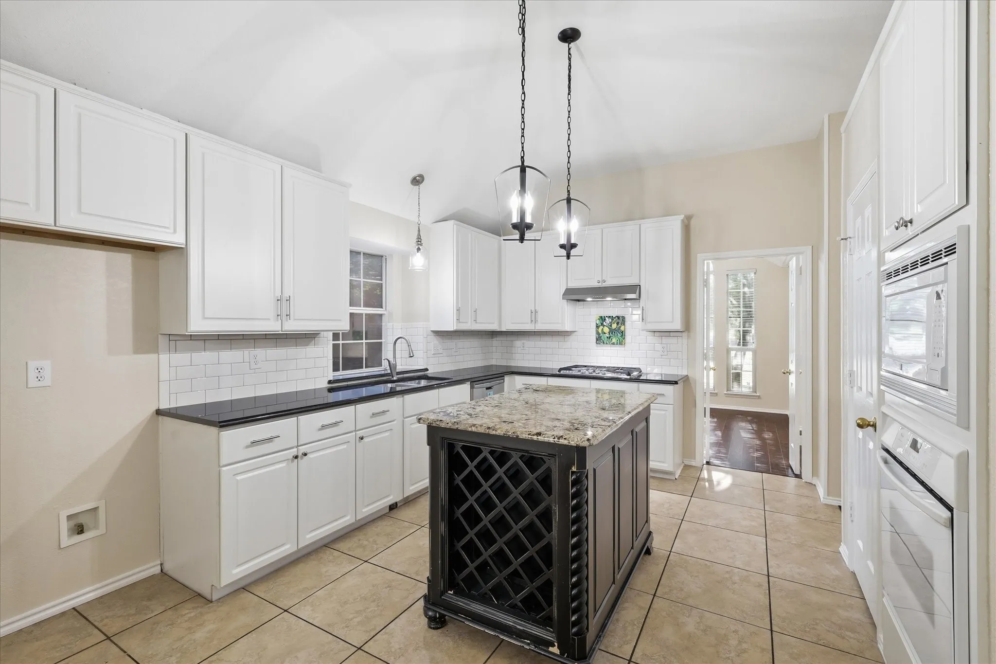 Light-filled kitchen featuring white cabinetry, dark countertops, tile flooring, a central island with wine storage, and built-in appliances