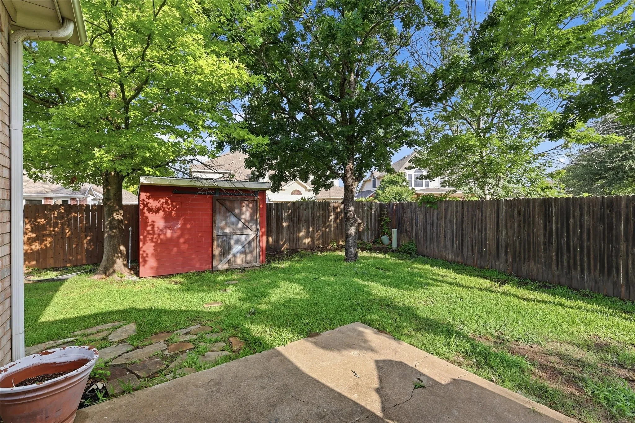 Expansive backyard featuring a manicured lawn, established trees, and a red storage shed