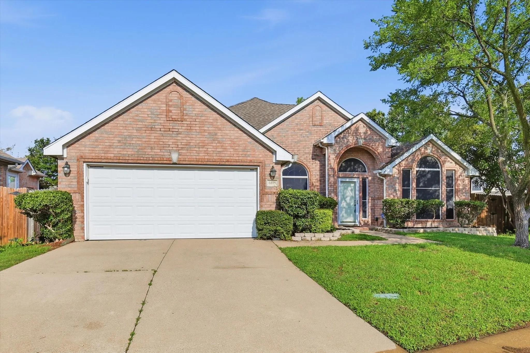 Brick exterior with a prominent arched entry, an attached two-car garage, multiple arched windows, and a mature tree