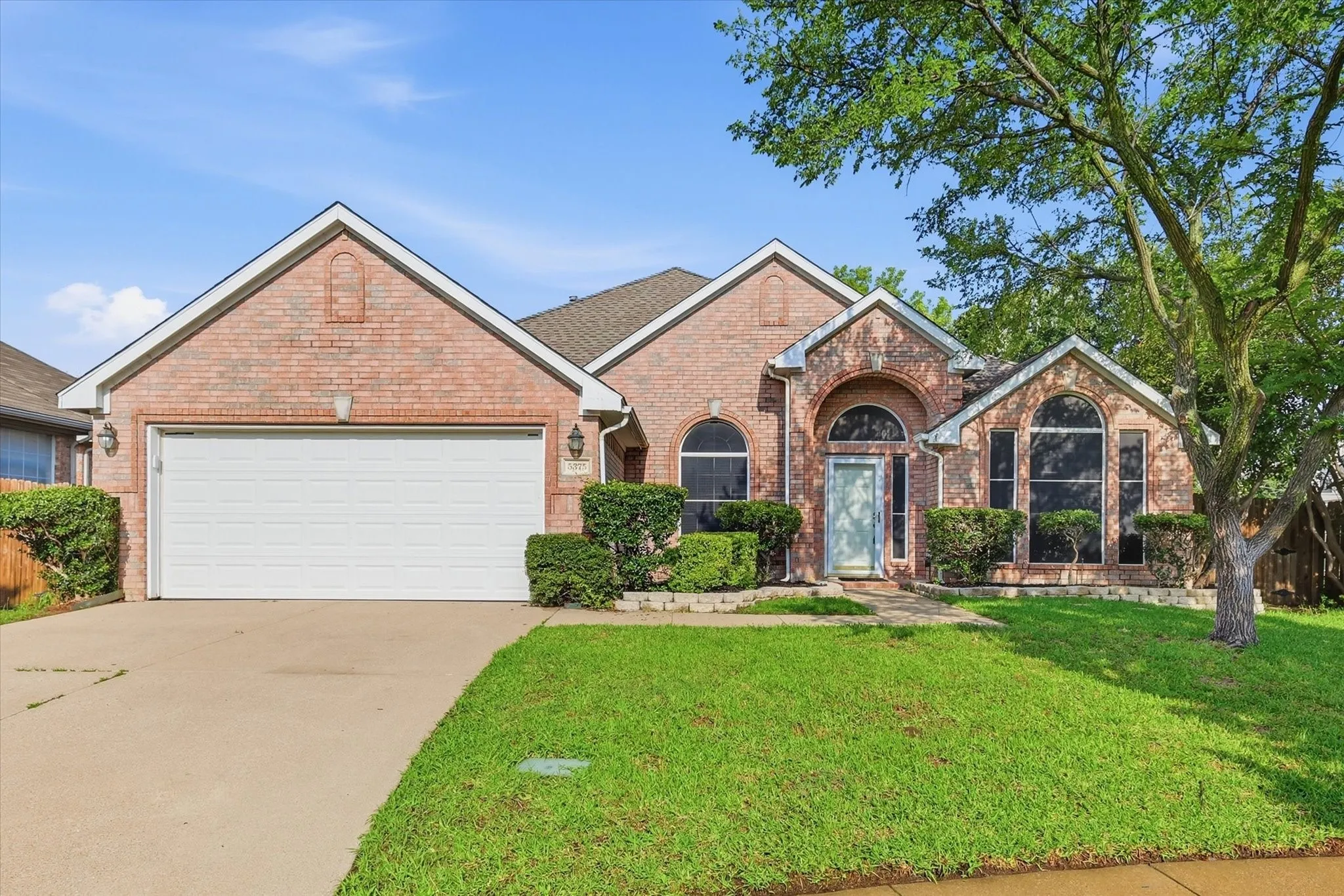 Red brick facade home featuring an attached garage, arched windows, and a concrete driveway