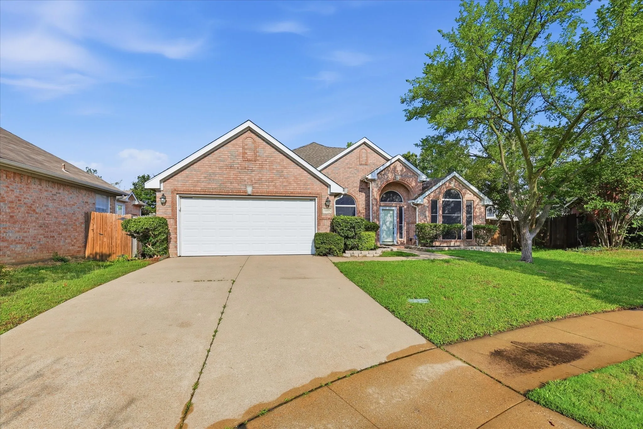 Brick facade residence with a two-car garage, concrete driveway, and established landscaping