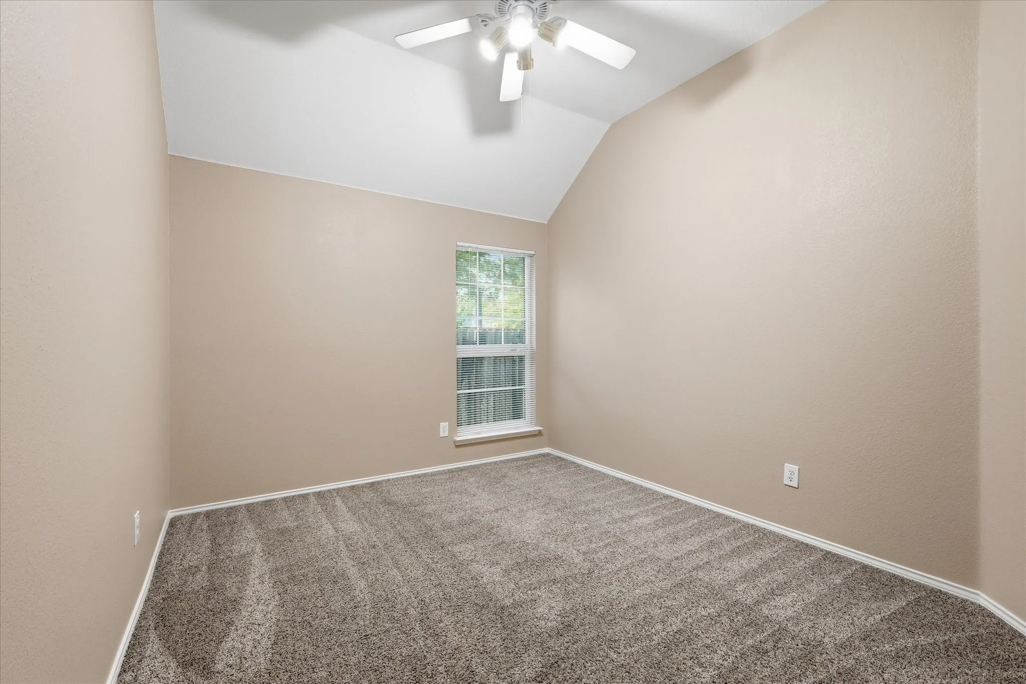 Carpeted room featuring a vaulted ceiling and a ceiling fan with light fixture