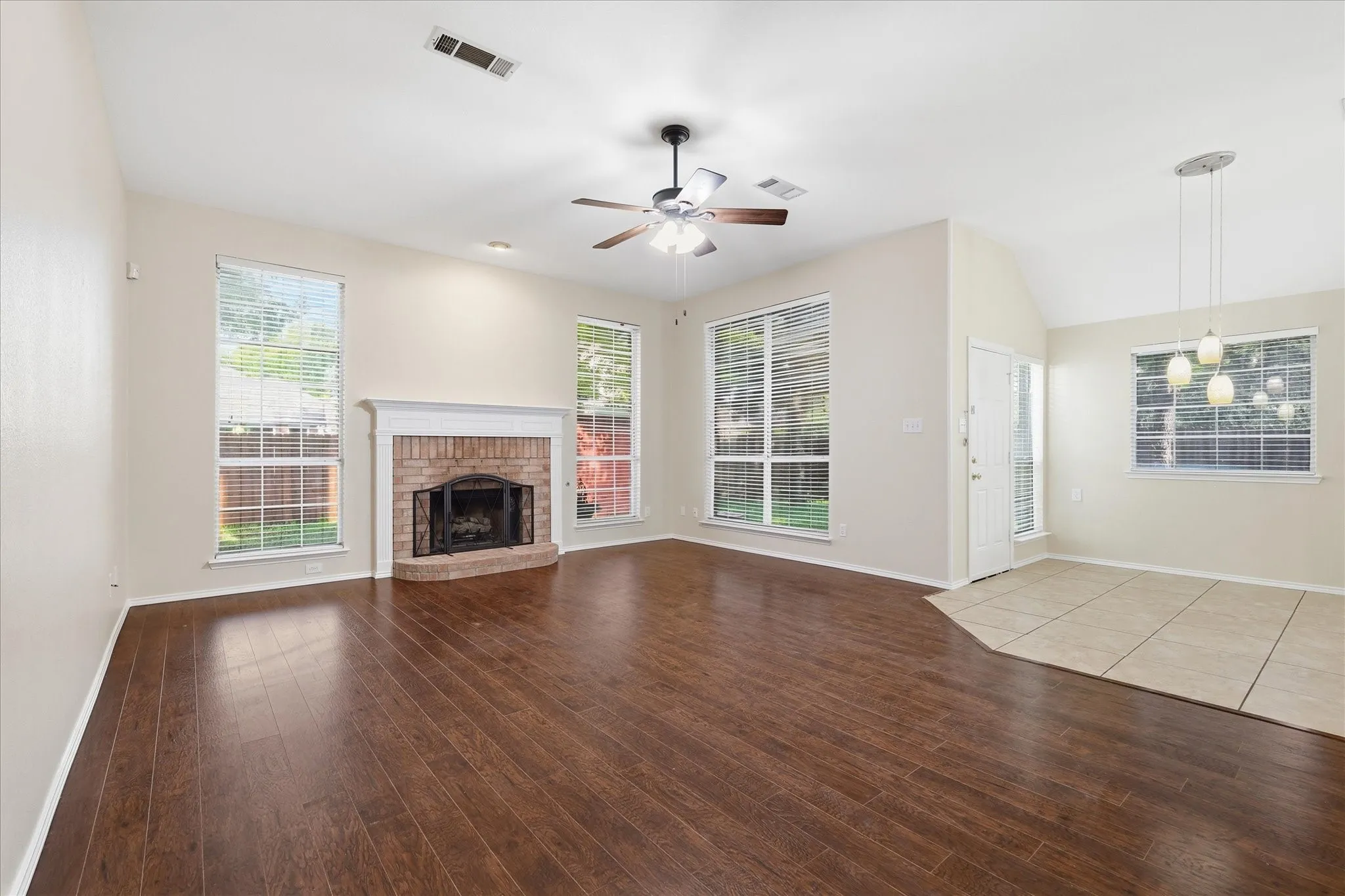 Spacious living area featuring wood-finish flooring, a brick fireplace with a white mantel, and multiple large windows