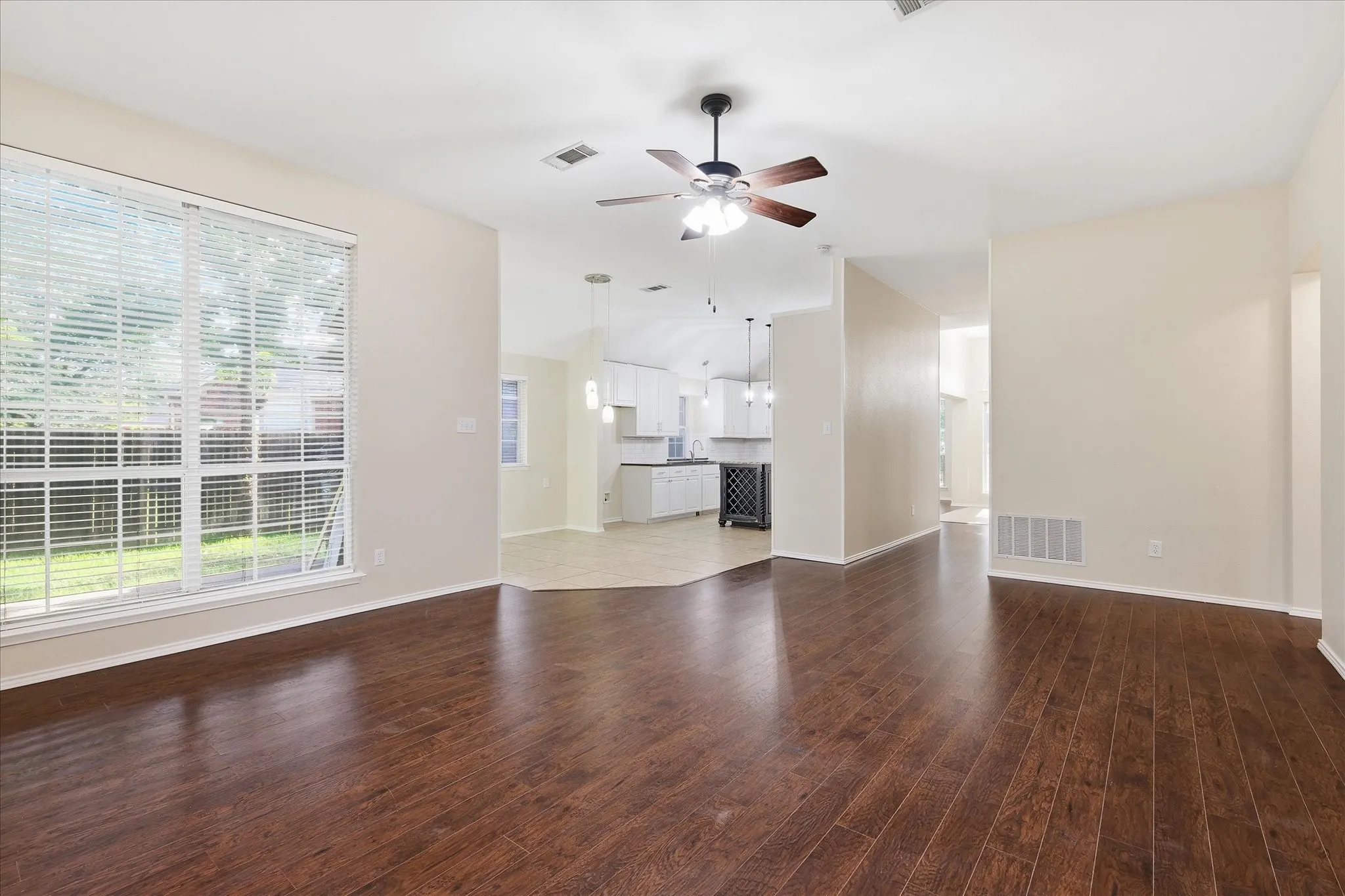 Spacious interior with wood-finish flooring, a large window with horizontal blinds, and a ceiling fan