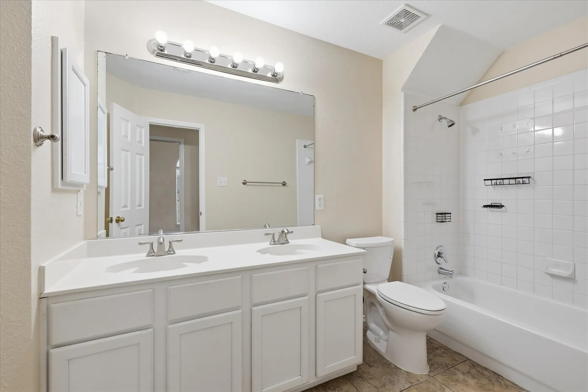 Bathroom featuring a dual-sink vanity with white cabinetry, a large mirror, and a chrome light fixture