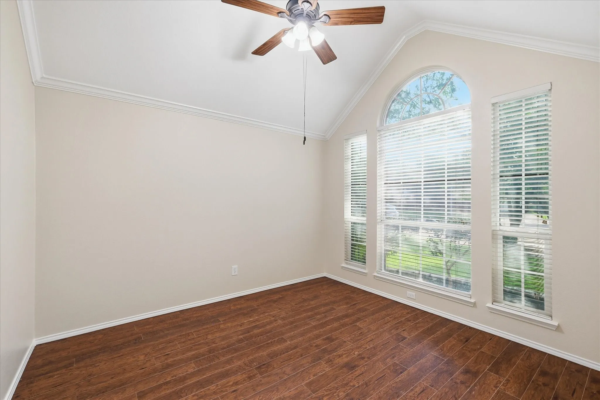 Vaulted ceiling room featuring a large arched window, two additional vertical windows, wood-finish flooring, and a ceiling fan with light fixture