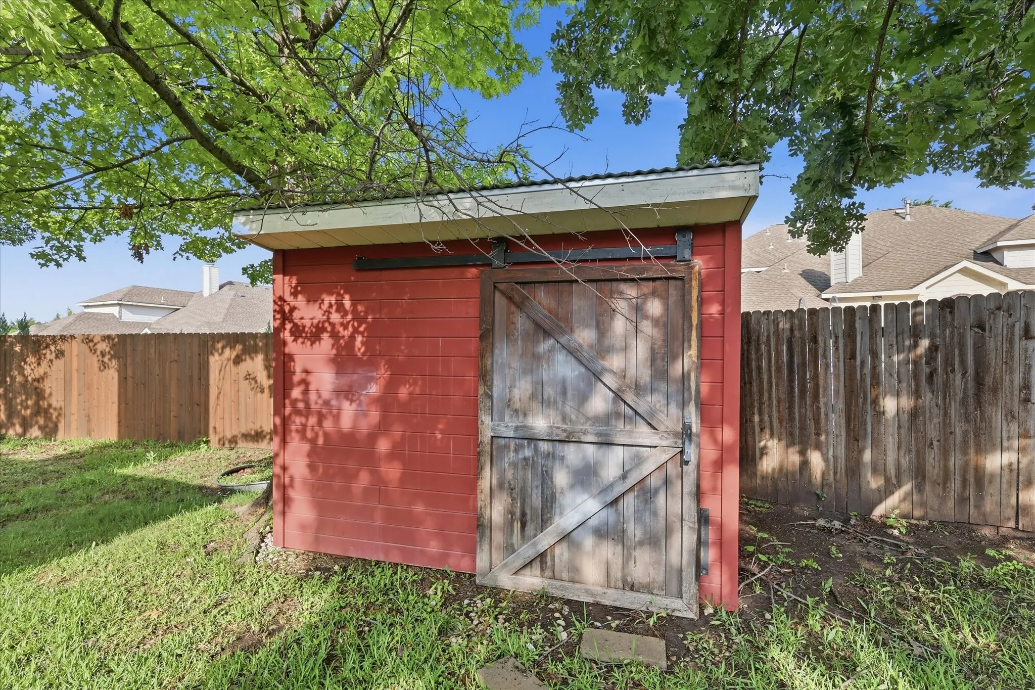 Red-painted storage shed with a rustic wood barn door and a metal roof