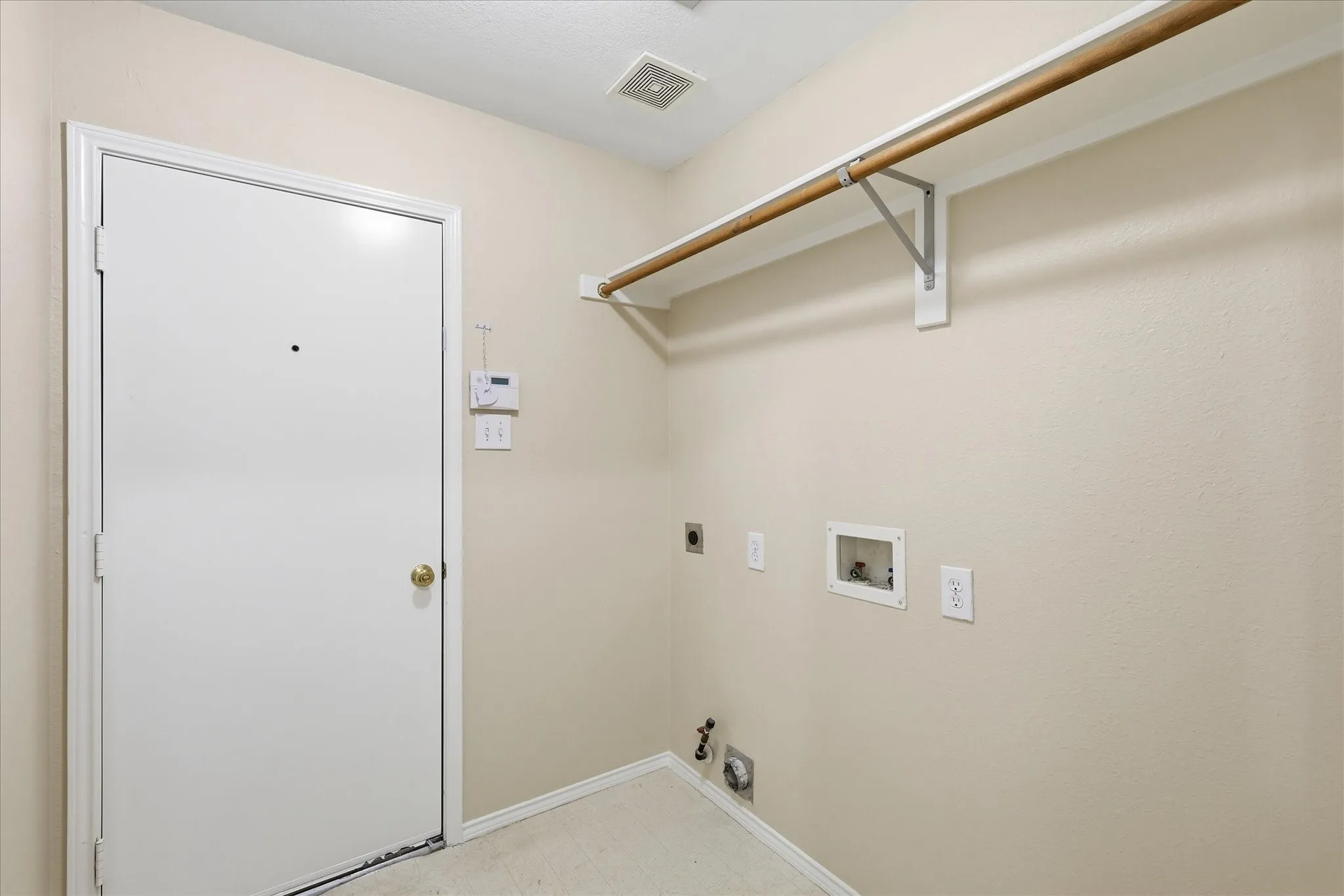 Laundry space featuring a white door, light neutral wall paint, and a built-in hanging rod
