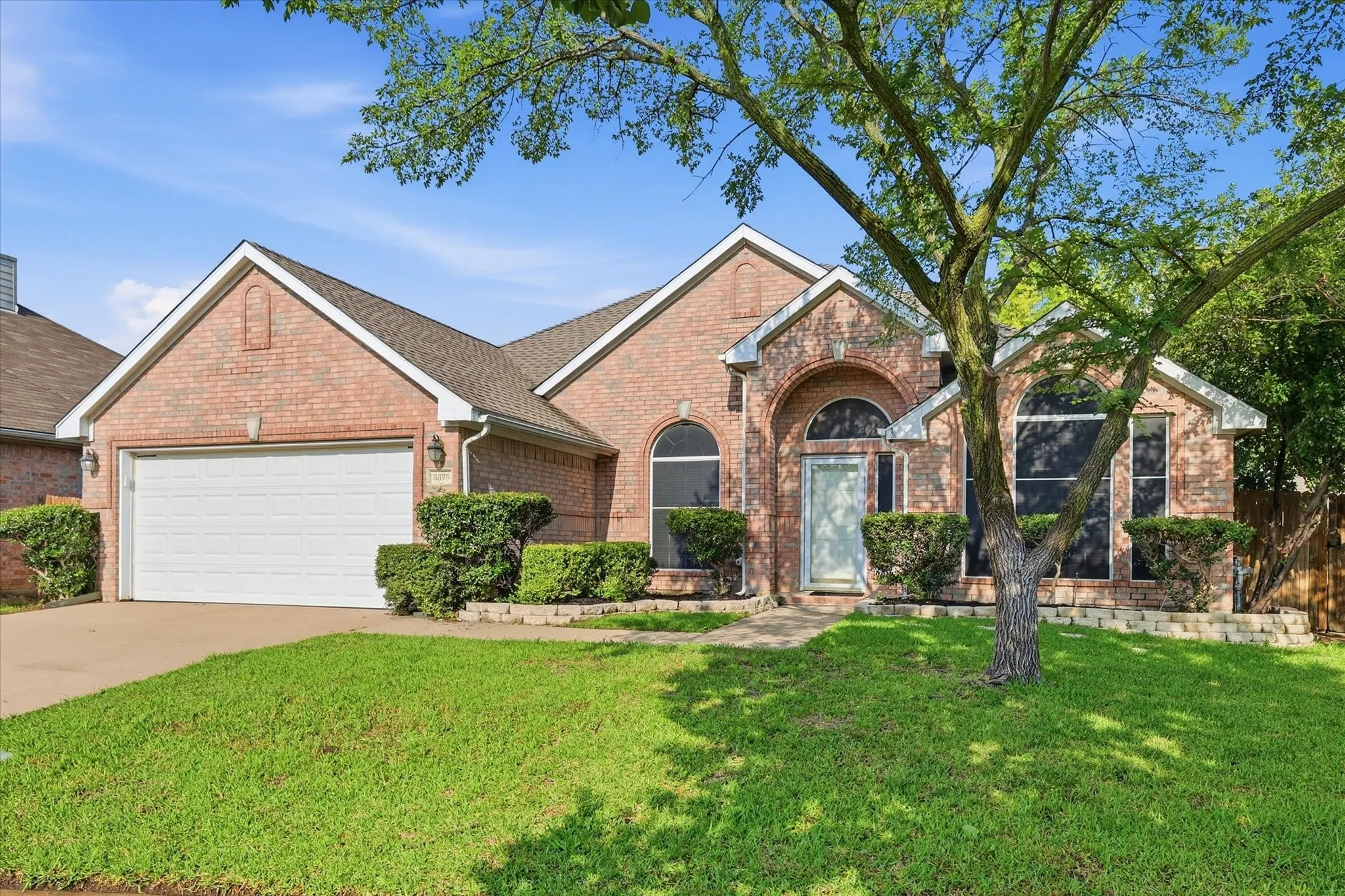 Brick exterior featuring a two-car garage, arched entryways, and mature landscaping