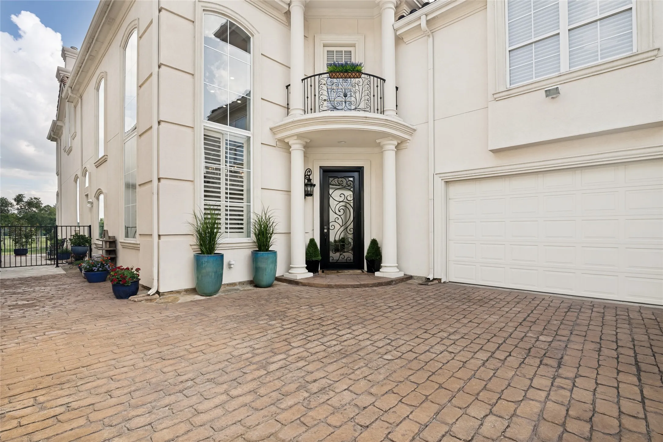 Stucco exterior featuring a stamped concrete driveway, arched windows with shutters, a decorative wrought-iron front door, and an upper-level balcony with a wrought-iron railing