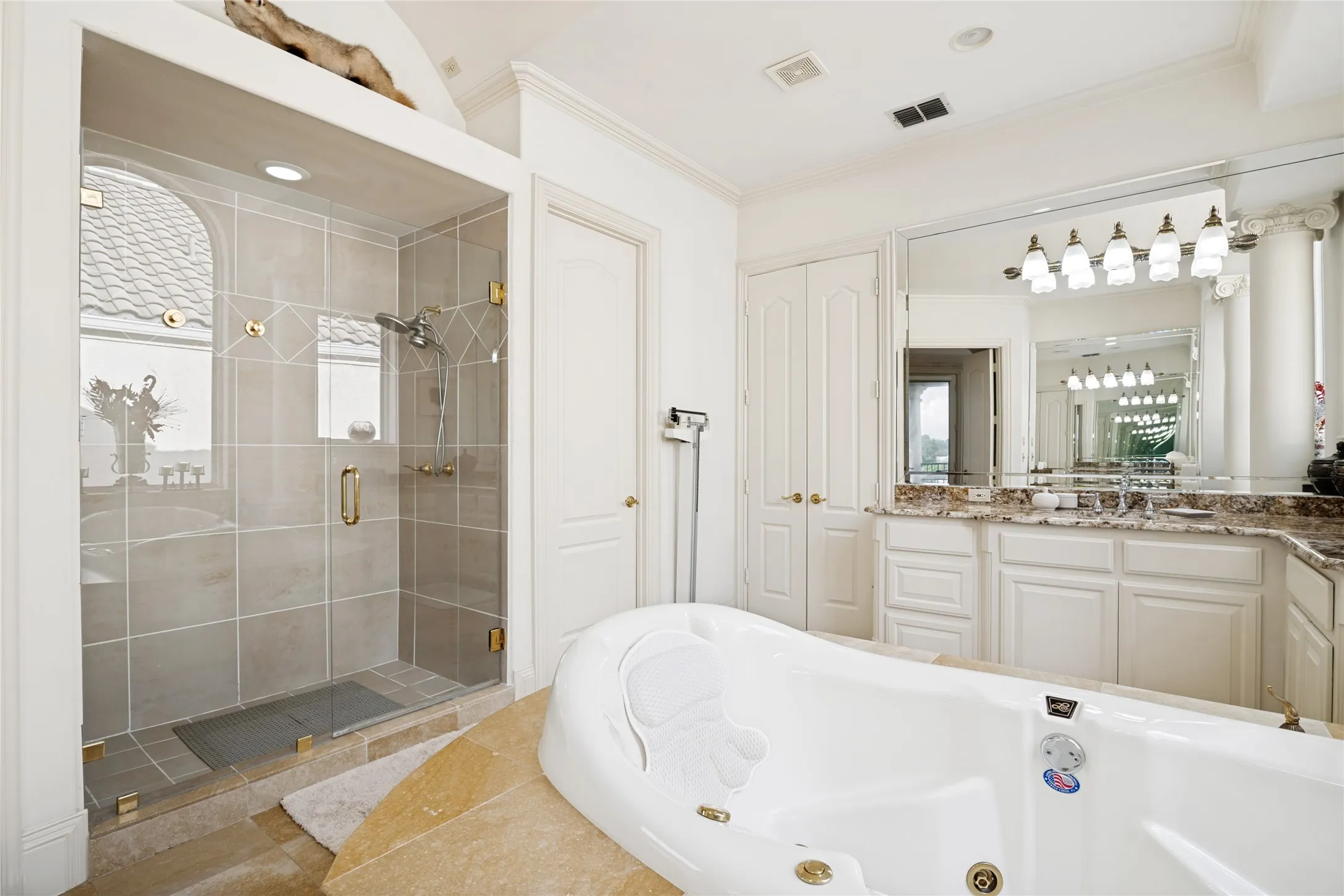 Spacious bathroom featuring a glass-enclosed shower with tile surround, a built-in jetted tub, a vanity with dual sinks, and extensive mirrored surfaces
