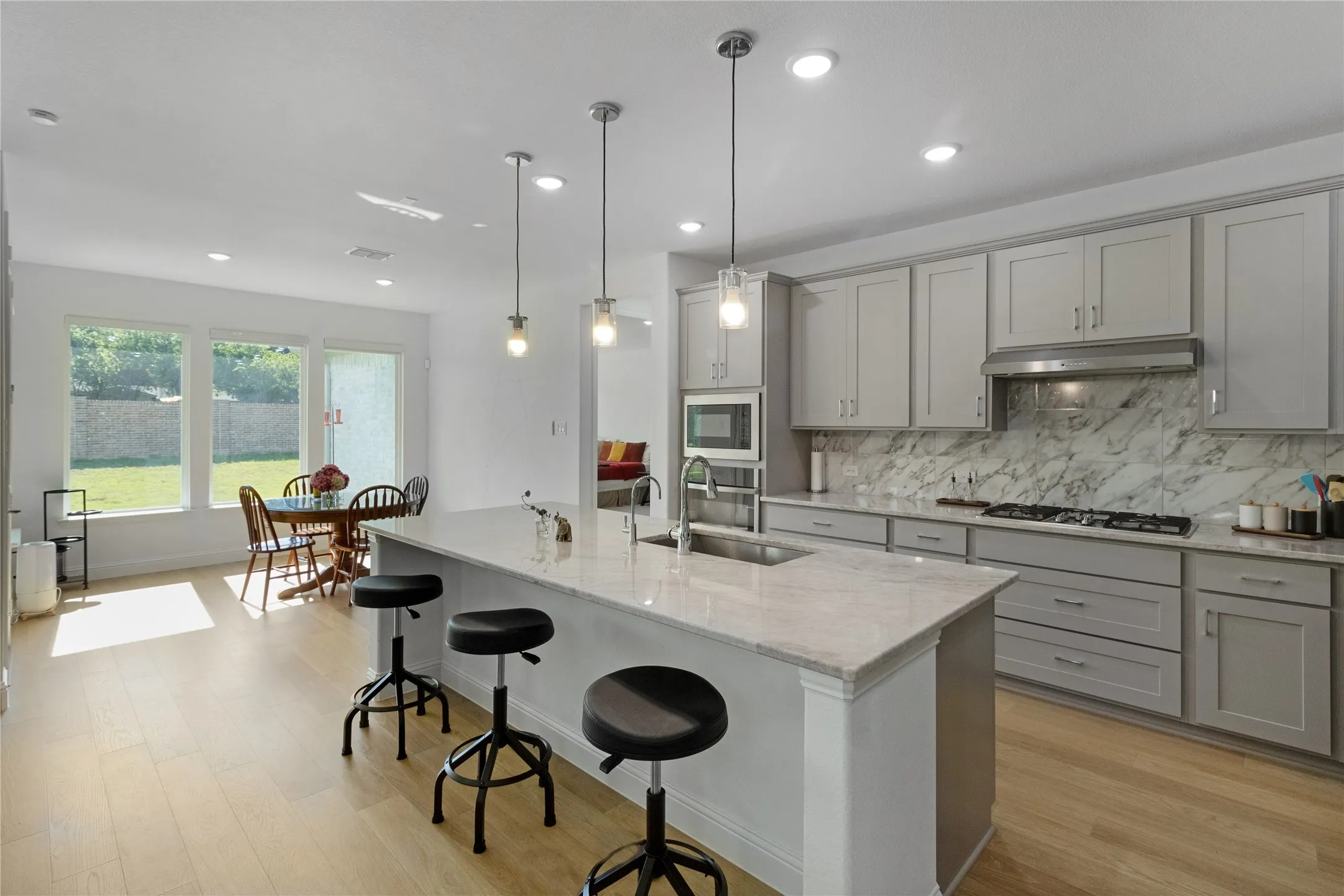 Contemporary kitchen featuring light gray cabinetry, a gas cooktop, built-in microwave, and a large central island with an integrated sink