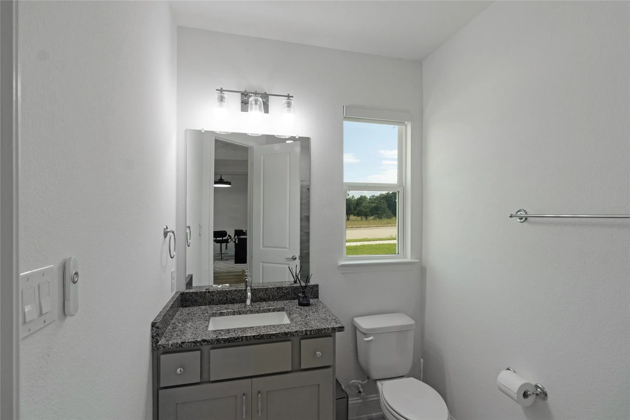 Bathroom featuring a granite-look countertop vanity with gray cabinetry, undermount sink, and a framed mirror
