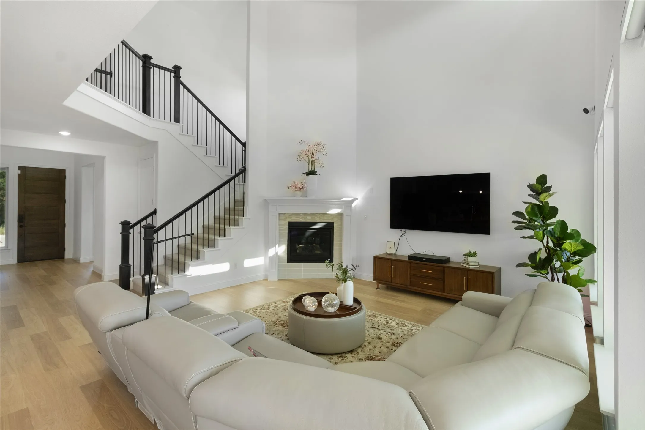 Two-story living area featuring wood-finish flooring, a contemporary fireplace with a stone surround and white mantel, and a multi-level staircase with dark wood newel posts and black iron balusters