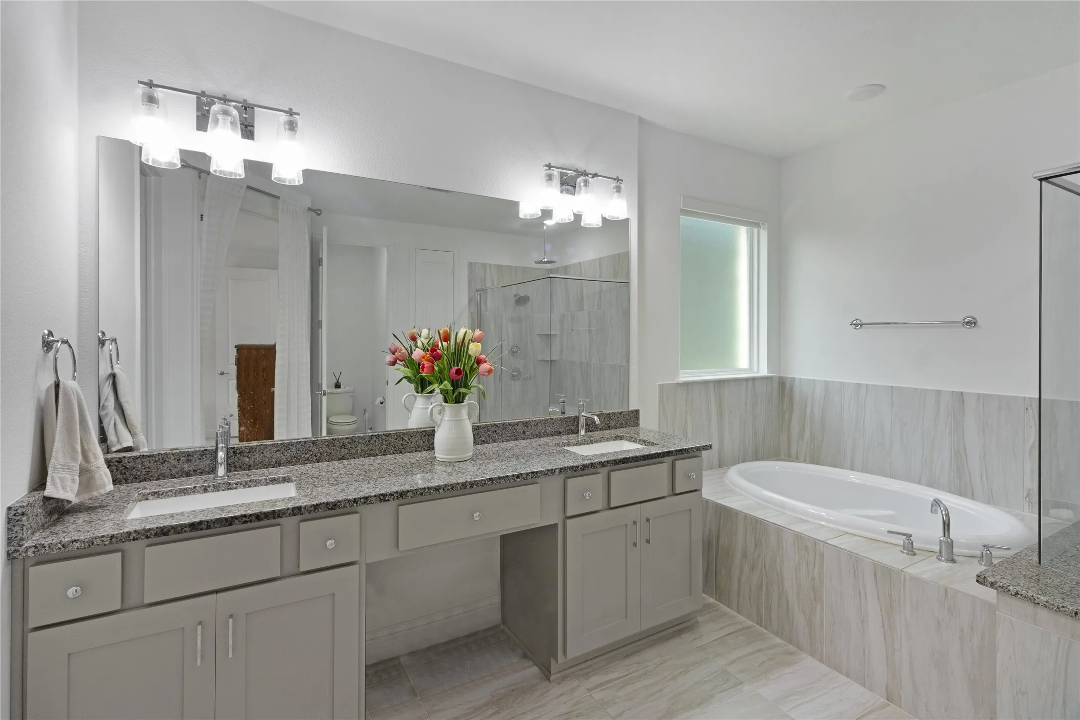 Spacious bathroom featuring a built-in oval soaking tub, large vanity with dual sinks, stone countertops, and tile flooring