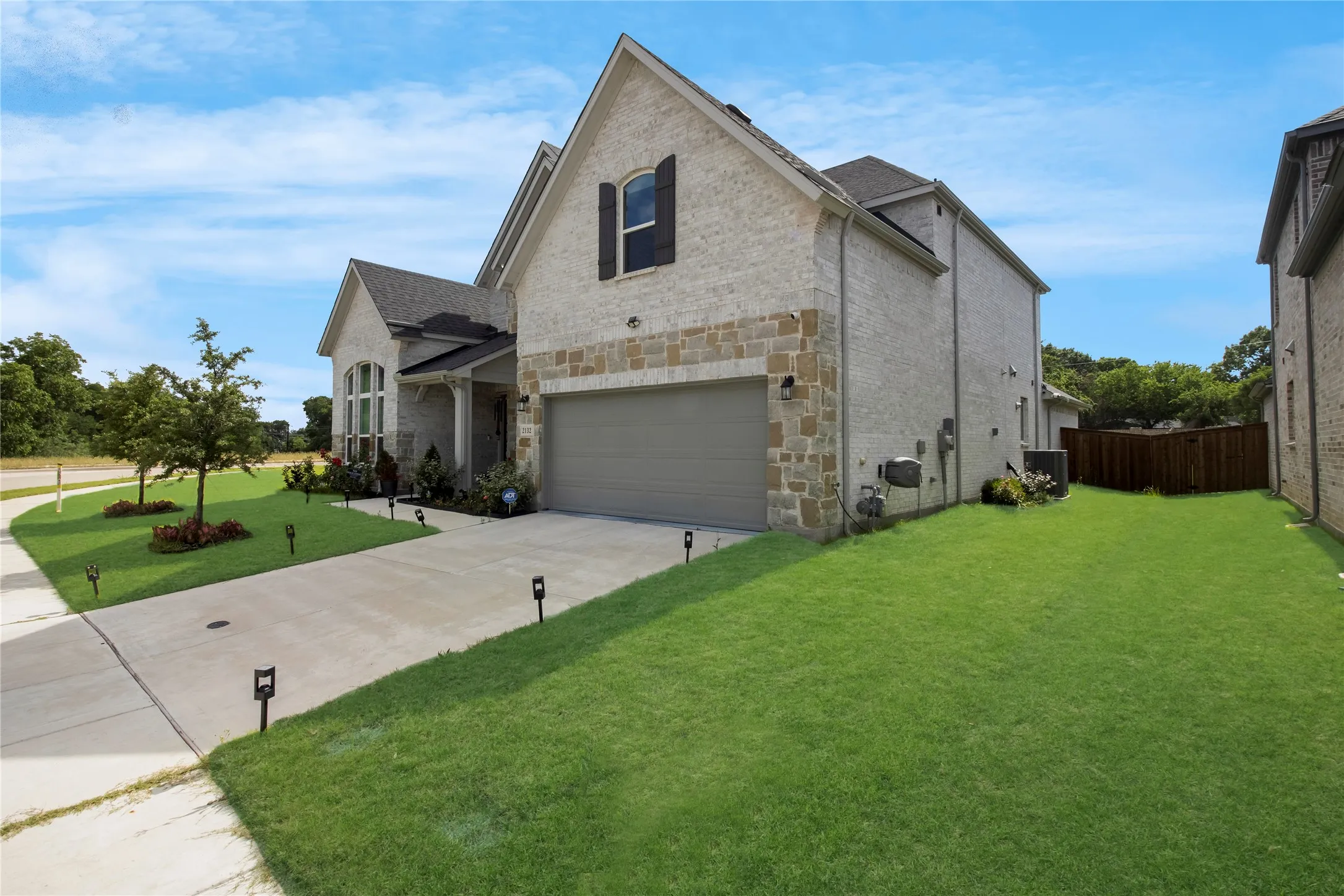 Brick and stone exterior with an attached garage, featuring a concrete driveway with integrated landscape lighting, a covered entryway, and a manicured lawn