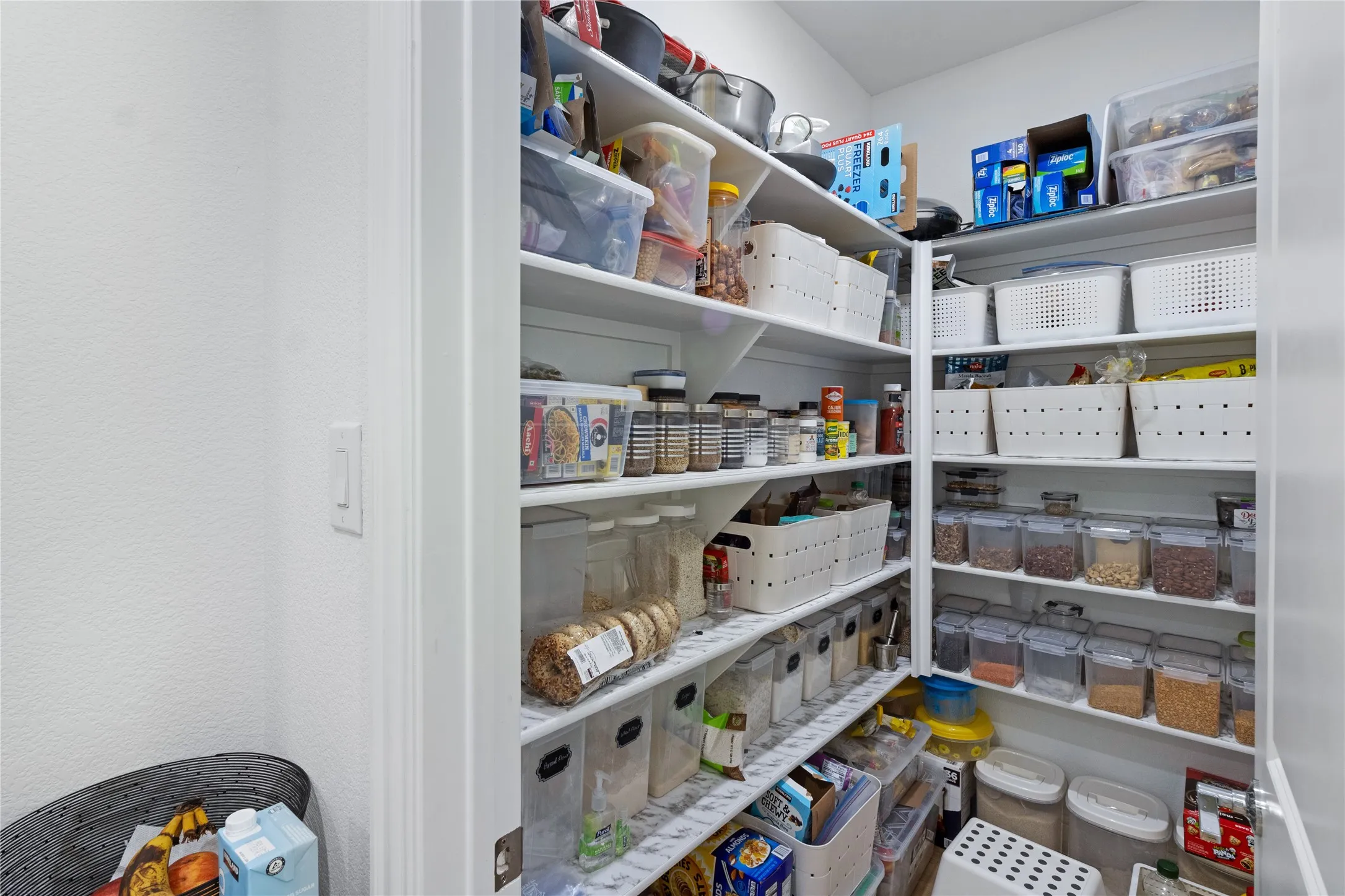 Spacious pantry featuring multiple tiers of built-in shelving, white painted walls, and a white door frame