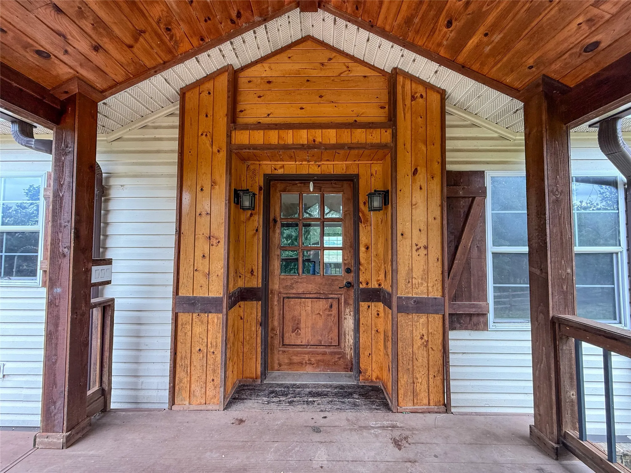 Inviting front porch featuring a wood-panel accent wall, wood-finish ceiling, and matching wood-paneled entry door with glass inserts