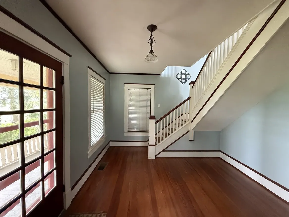 Entryway featuring wood-finish flooring, a classic staircase with dark wood handrails, a paneled door with multiple glass lites, and crisp white trim against light blue walls