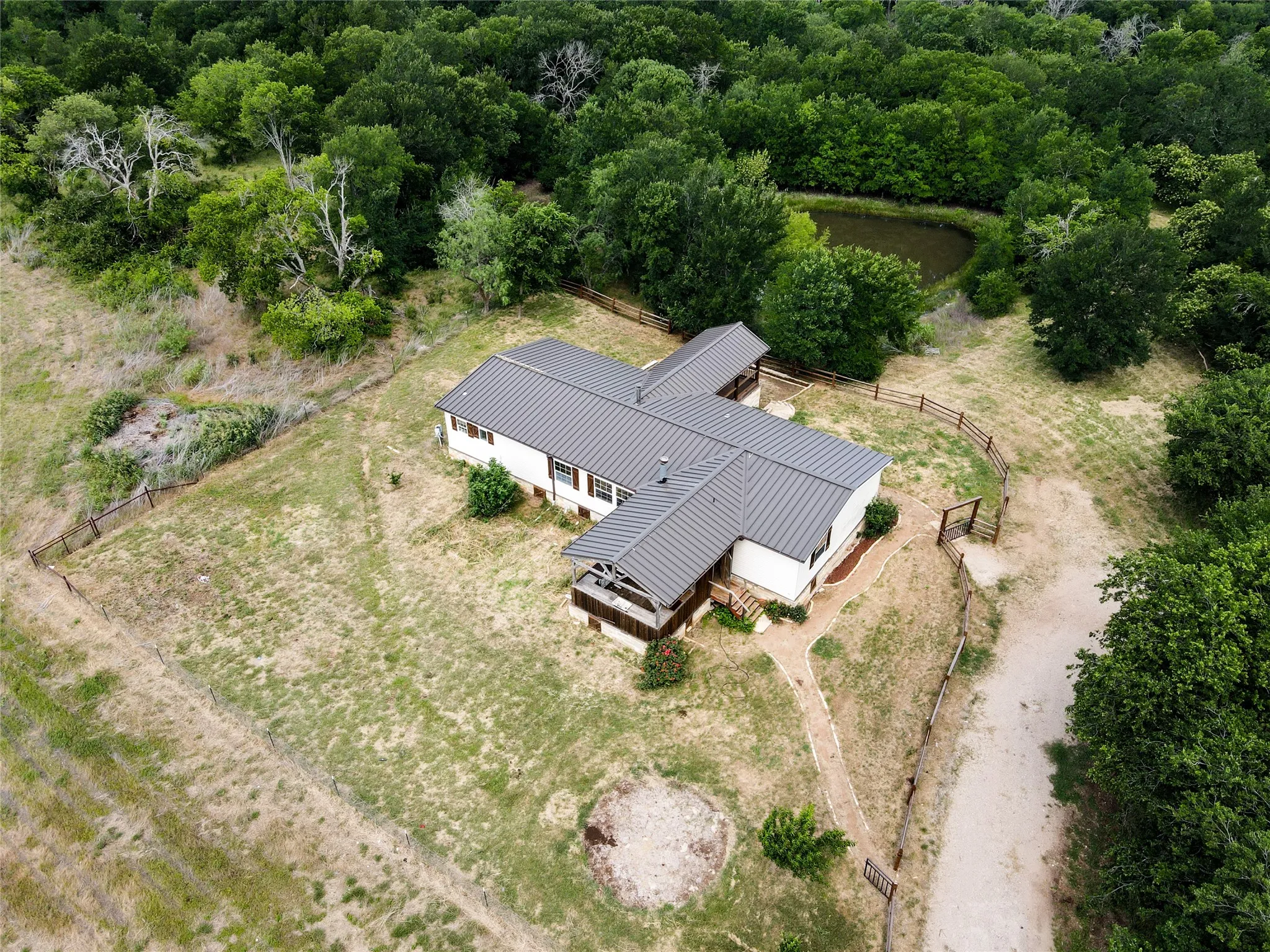Aerial property perspective featuring a white-sided residence with a gray metal roof, surrounded by mature trees