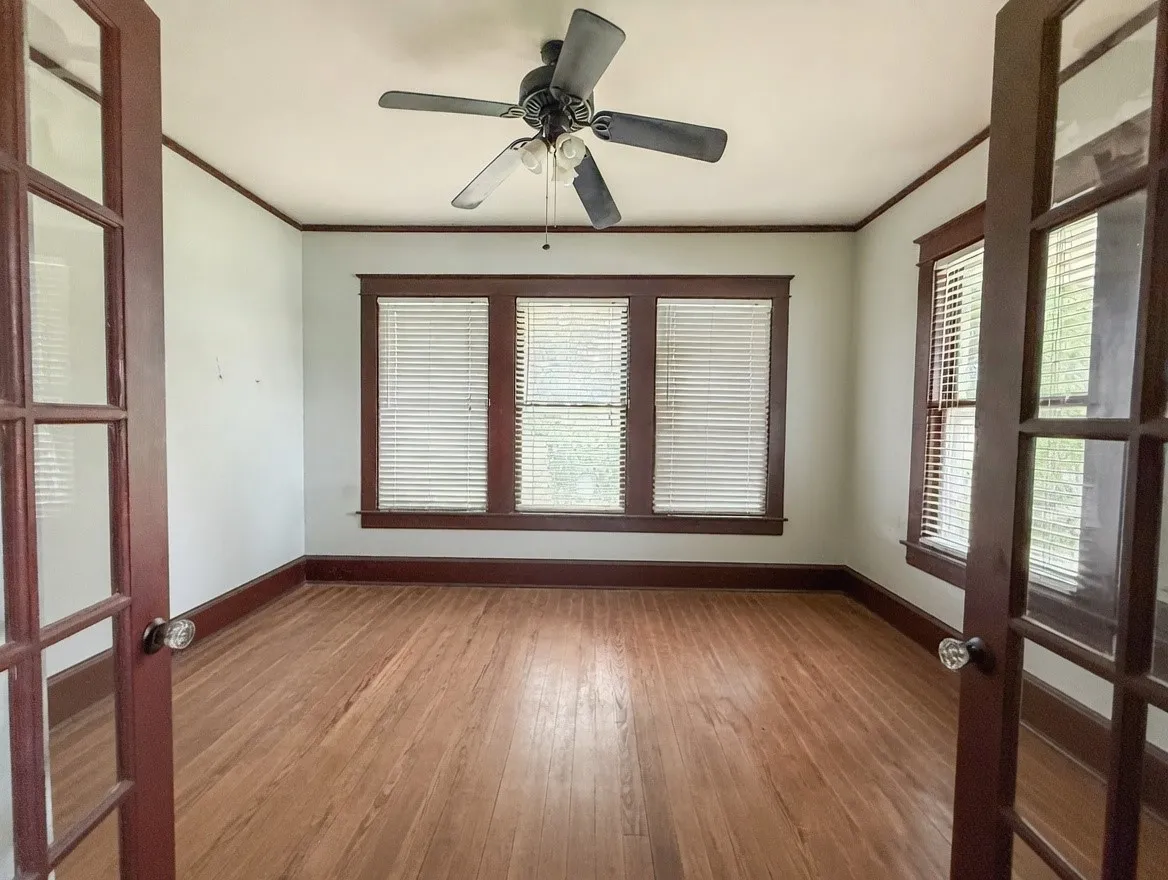Room featuring wood-finish flooring, dark wood trim, and a ceiling fan