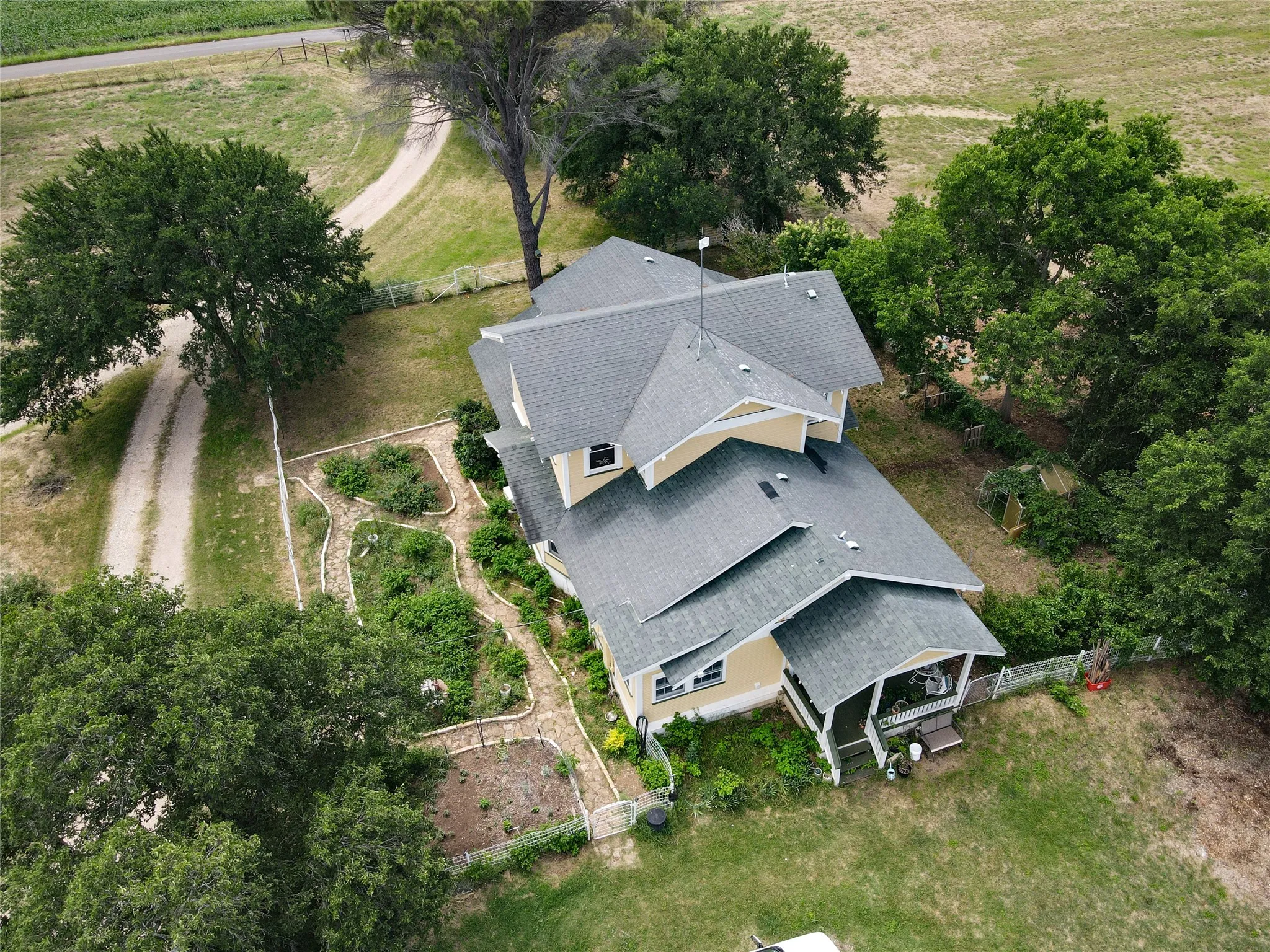 Expansive property featuring a two-story residence with a covered porch, established trees, and multiple garden beds