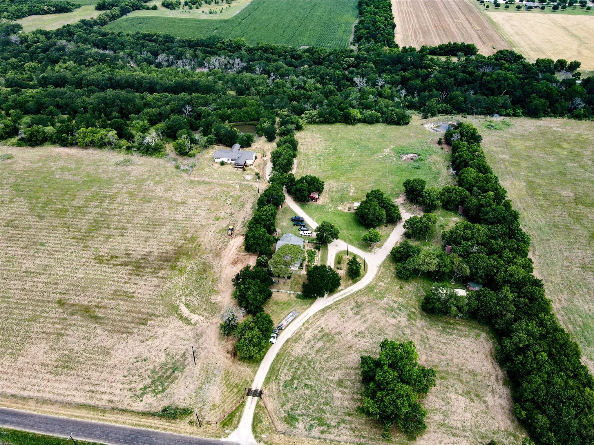 Expansive rural property featuring multiple cleared areas, established tree lines, a single-story residence, and a pond