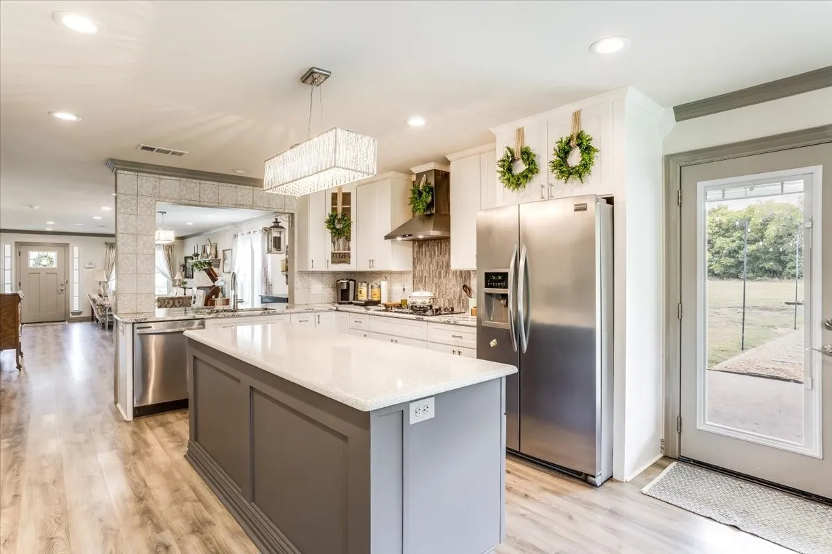 Open-concept kitchen featuring an island with a white countertop, wood-finish flooring, white cabinetry, and stainless steel appliances