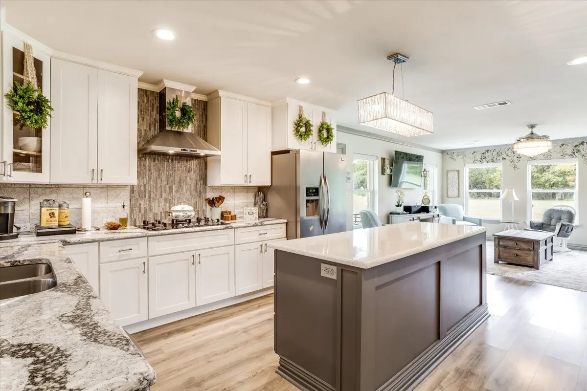 Open-concept kitchen featuring white cabinetry, light-toned countertops, a gas range with stainless steel hood, and a central island
