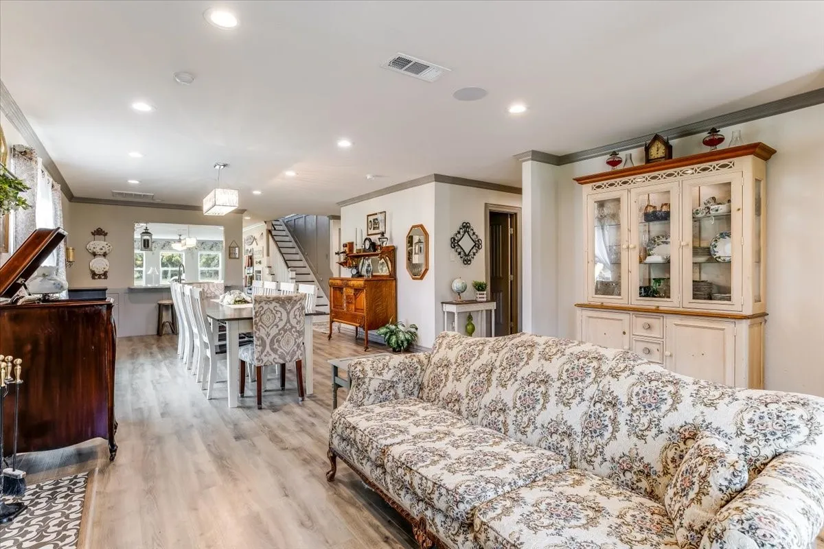Open-concept living space featuring wood-finish flooring, recessed lighting, crown molding, and a built-in display cabinet