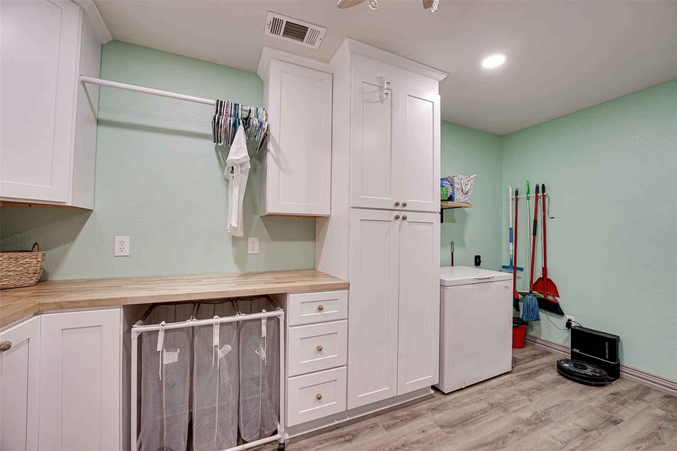 Dedicated utility room featuring abundant white shaker cabinetry, wood-finish countertops, a built-in hanging rod, and light wood-finish flooring