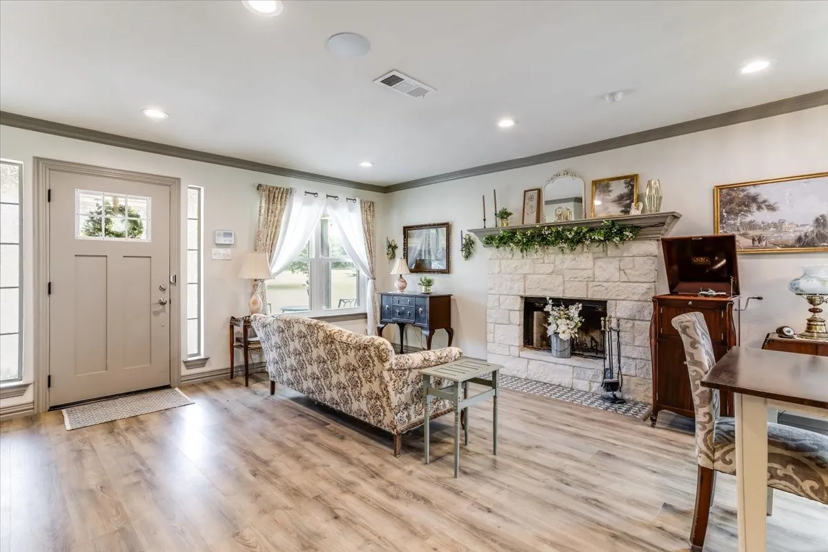 Living area featuring wood-finish flooring, a stone fireplace with a wood mantle, recessed lighting, and a front entry door with sidelights
