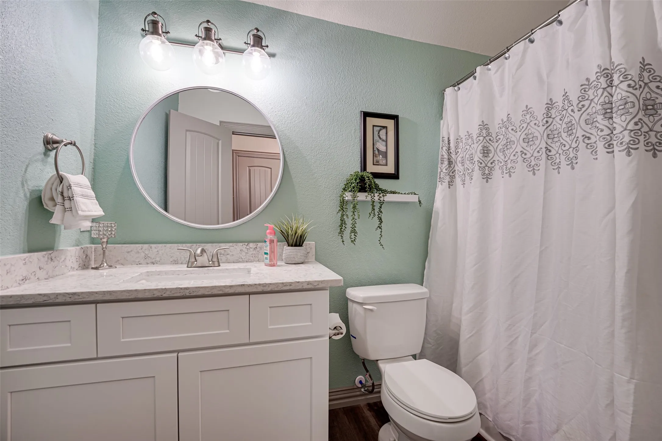 upstairs bathroom featuring a light blue-green wall color, white vanity with a light-toned countertop, and a round wall-mounted mirror
