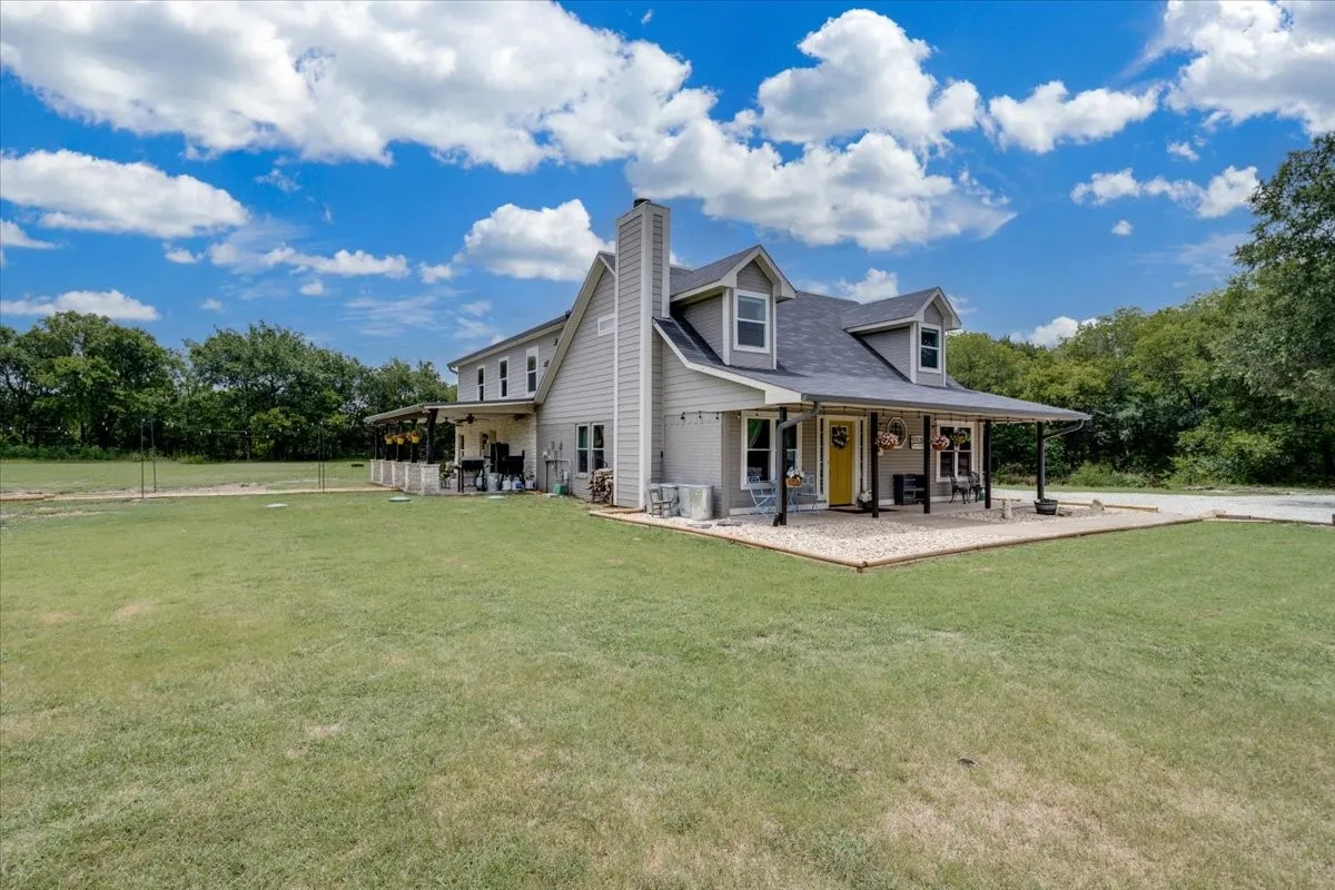 Modern farmhouse residence featuring a distinctive peaked roofline with dormer windows, complemented by a expansive covered carport with sturdy support posts