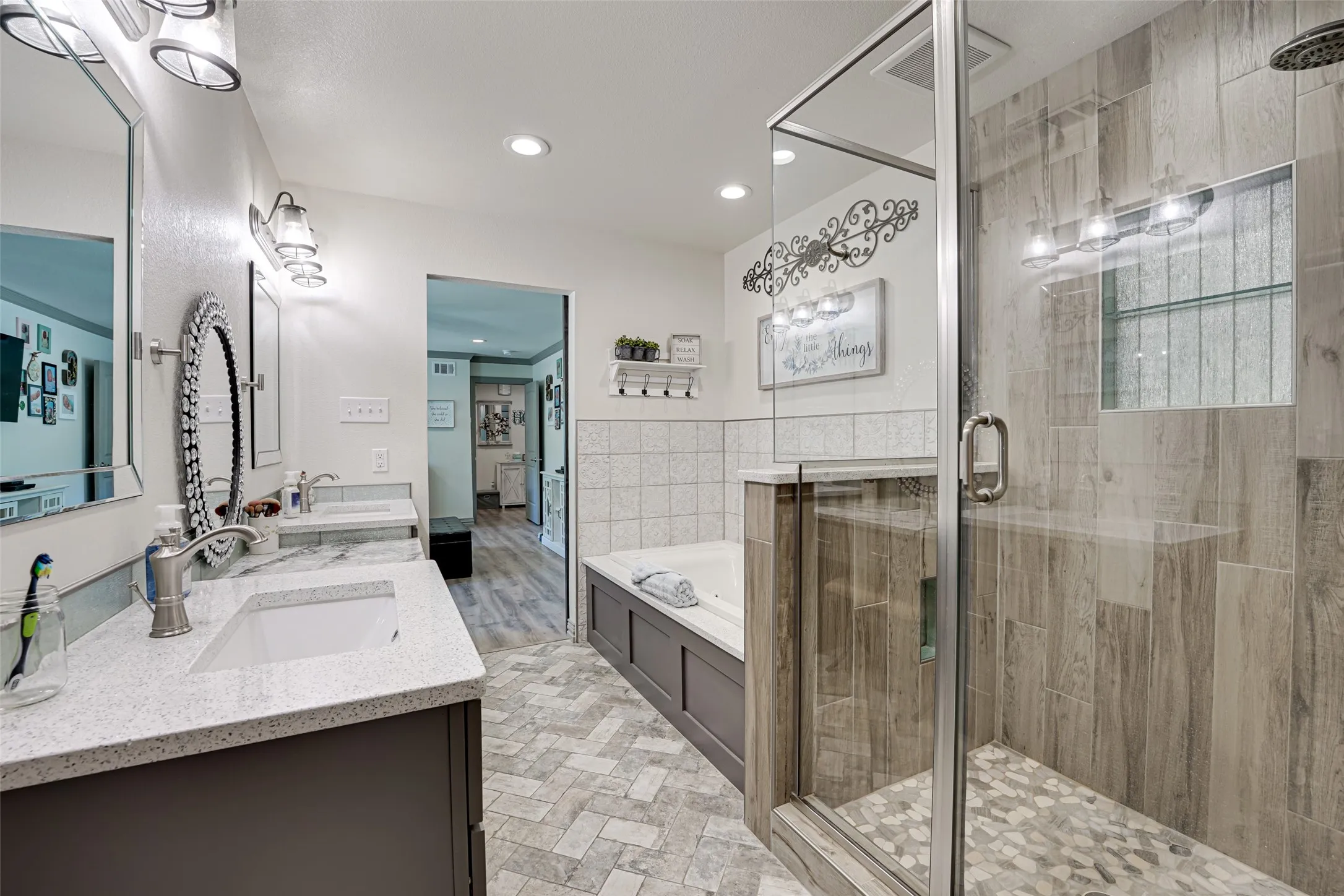 Spacious primary bathroom featuring a glass-enclosed shower with pebble tile flooring and wood-look tile surround