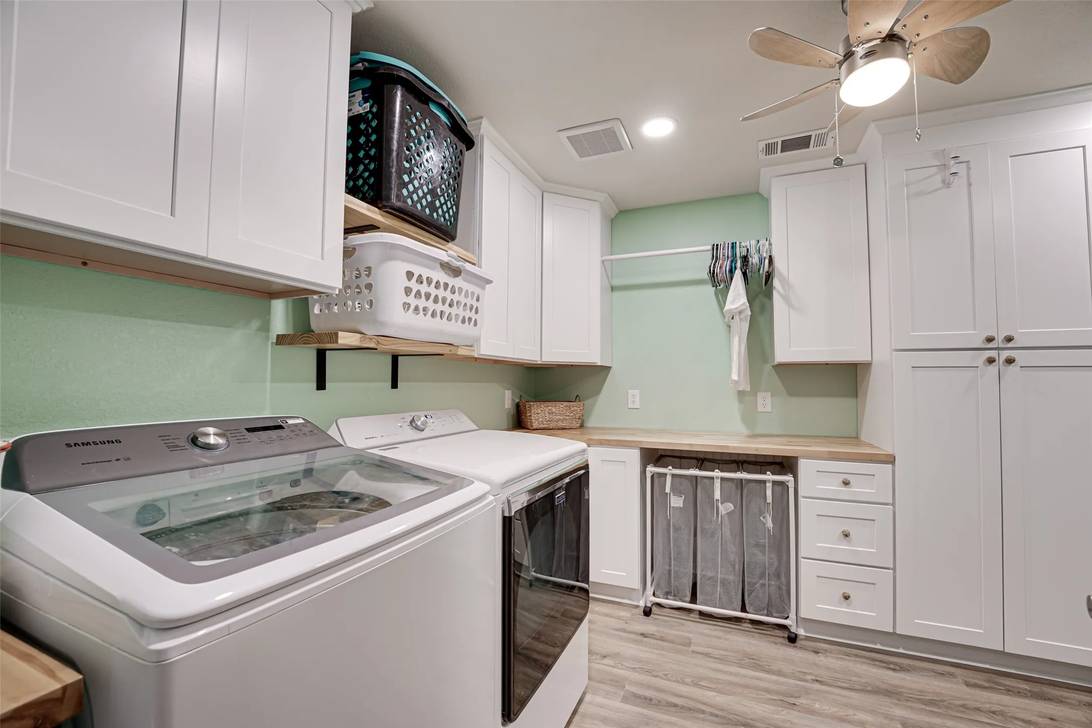 Dedicated laundry area featuring white shaker-style cabinetry, wood-finish countertops, and wood-finish flooring