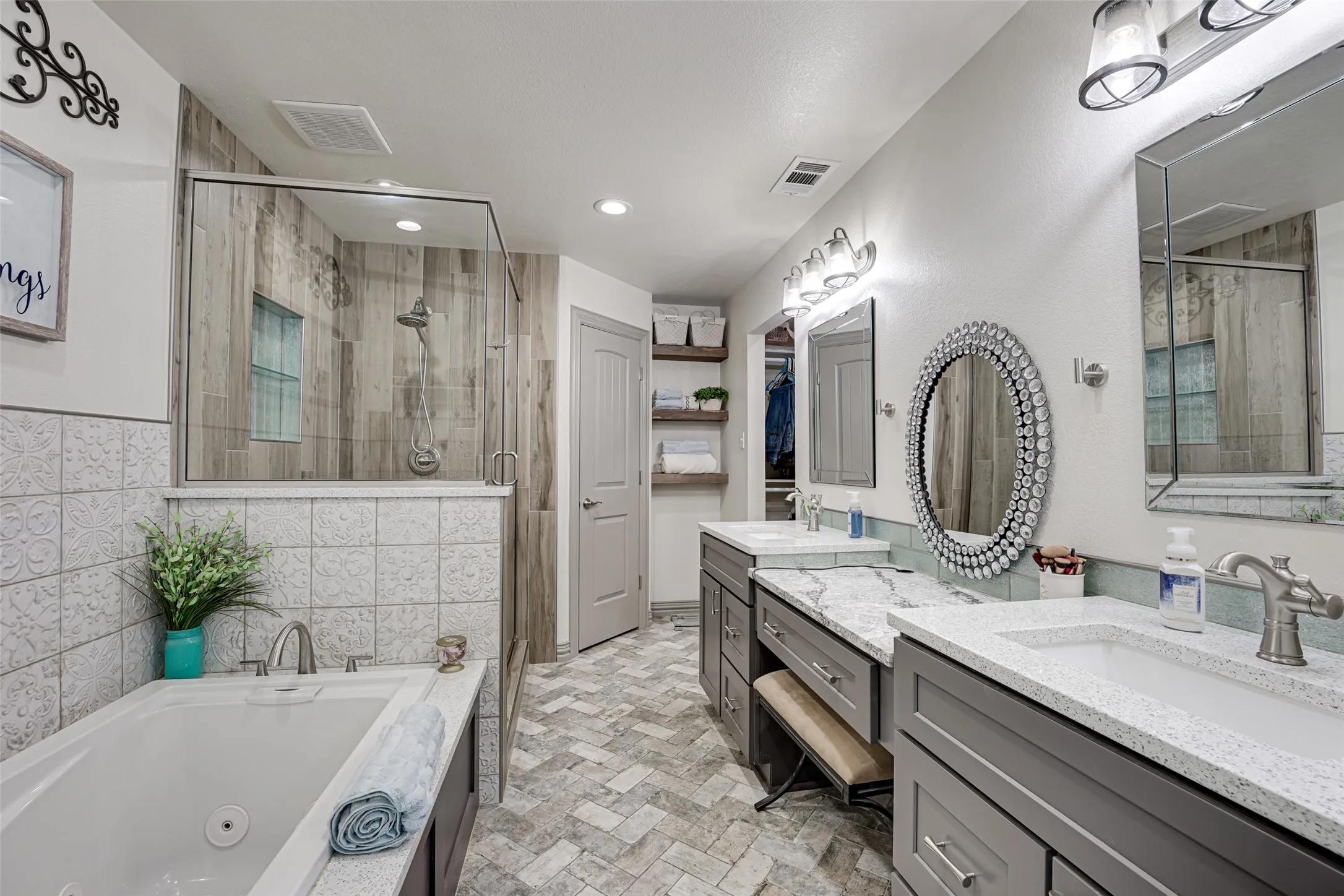Spacious primary bathroom featuring a built-in jetted tub, a glass-enclosed shower with wood-finish tile, and dual vanity sinks with light-colored countertops