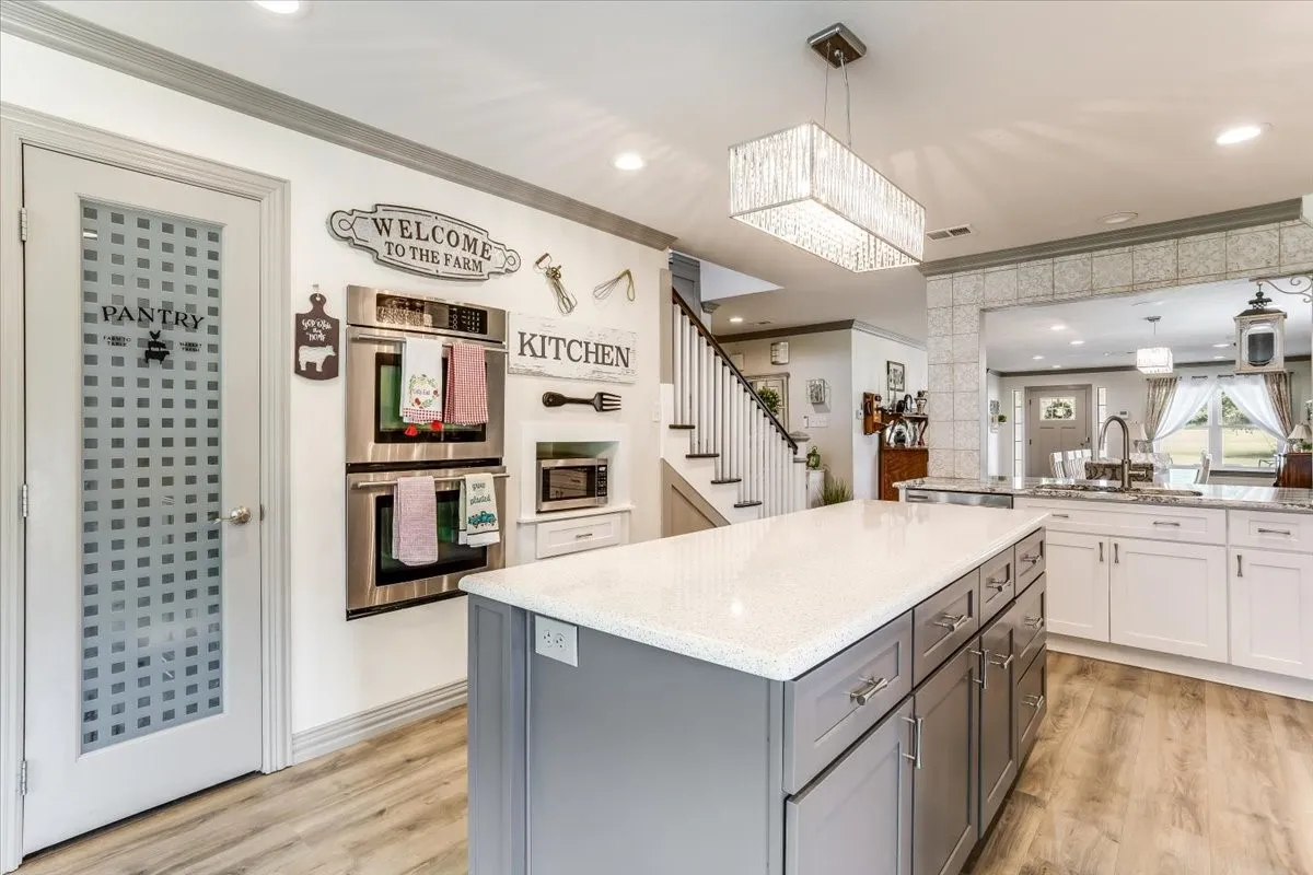 Kitchen featuring a large center island with a light-colored countertop, stainless steel double wall ovens, wood-finish flooring, and a decorative frosted pantry door